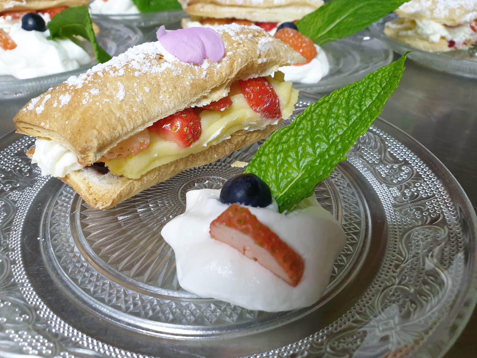 Postres: capes de pasta amb nata, maduixes i nabius en un plat de vidre, guarnides amb menta. Cal Serni