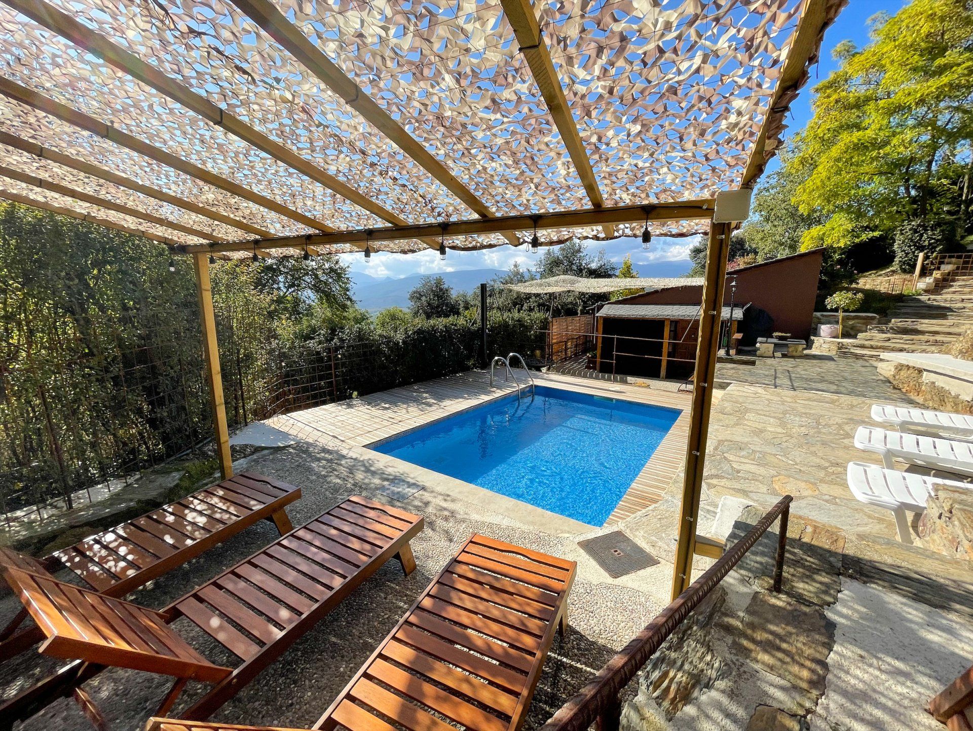 Piscina amb gandules de fusta sota una pèrgola a l'ombra, vistes a la muntanya. Cal Serni