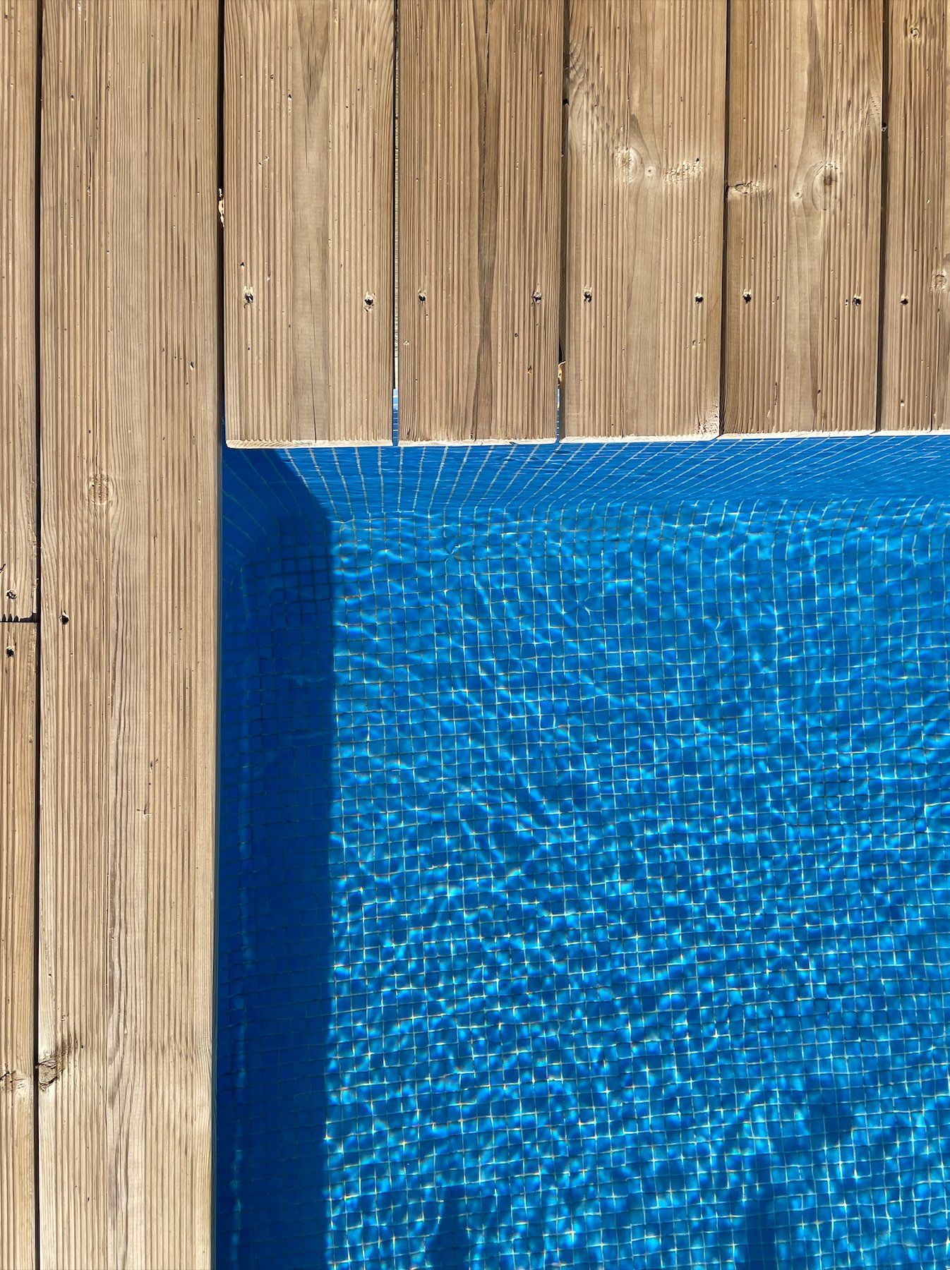 Racó de terrassa de fusta al costat d'una piscina plena d'aigua blava. Cal Serni