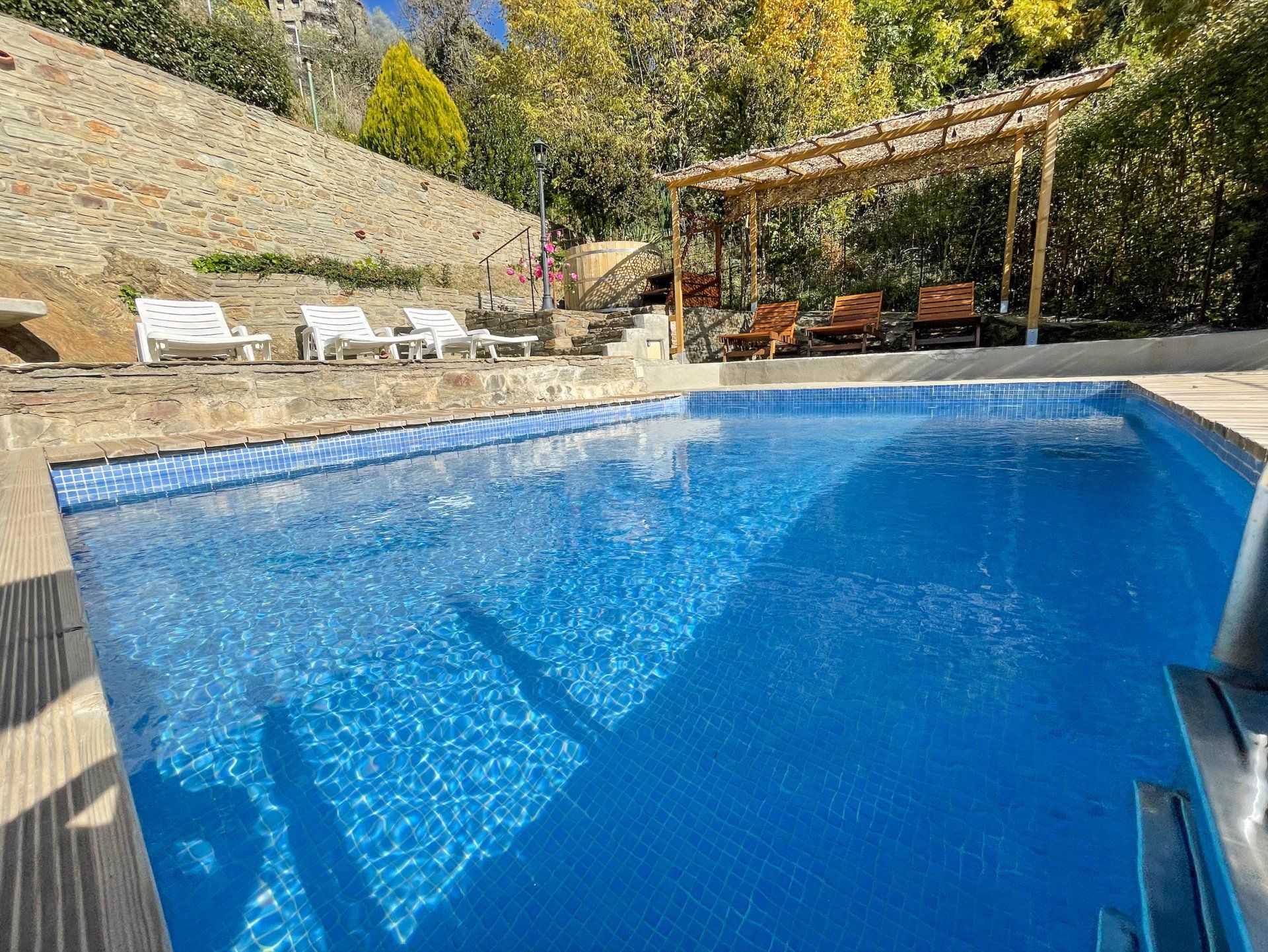 Piscina amb rajoles blaves, gandules i pèrgola en un entorn de vessant.