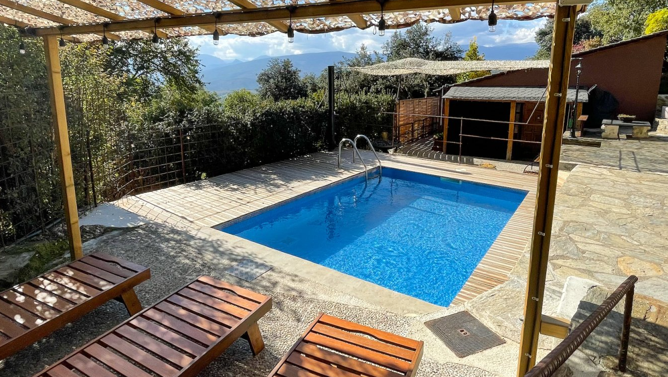 Petita piscina rectangular exterior amb aigua blava, envoltada de pedra. Gandules de fusta sota una pèrgola. Cal Serni