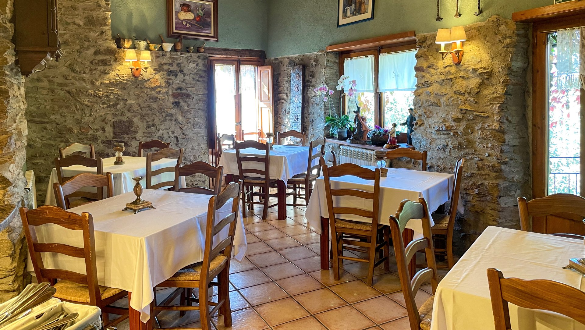 Interior de restaurant amb parets de pedra, terra de rajoles, estovalles blanques i cadires de fusta. Cal Serni