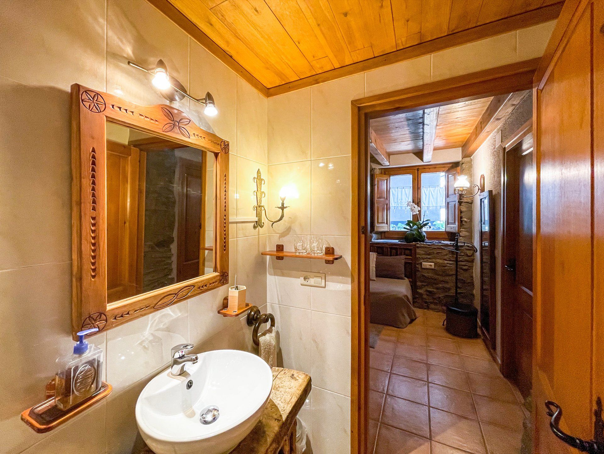 Bany amb elements de fusta, com ara un marc de mirall, sostre i portes. Un lavabo i vistes a un dormitori. Cal Serni