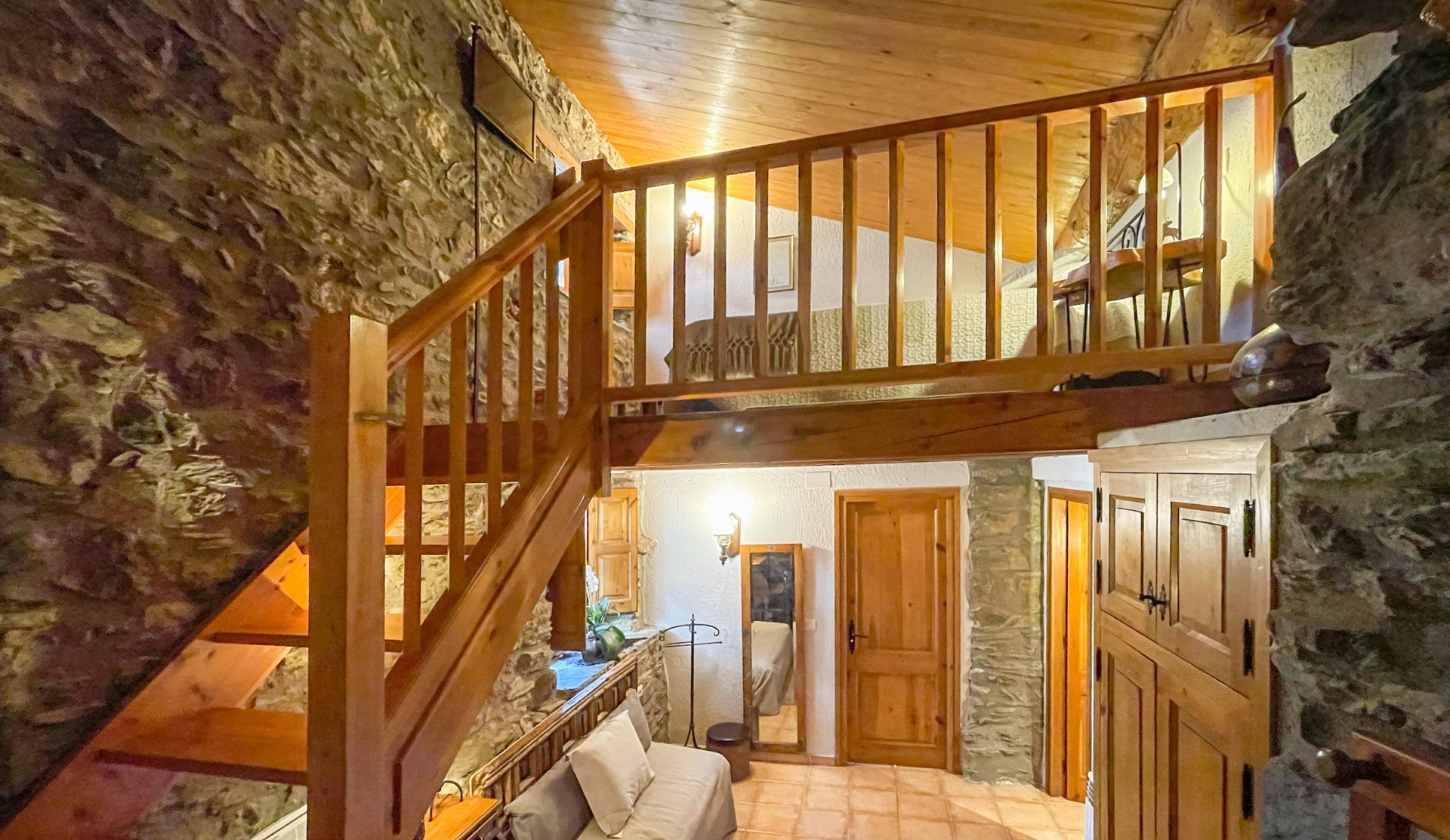Interior d'una habitació rústica amb una escala de fusta que condueix a un altell. Parets de pedra.  Cal Serni