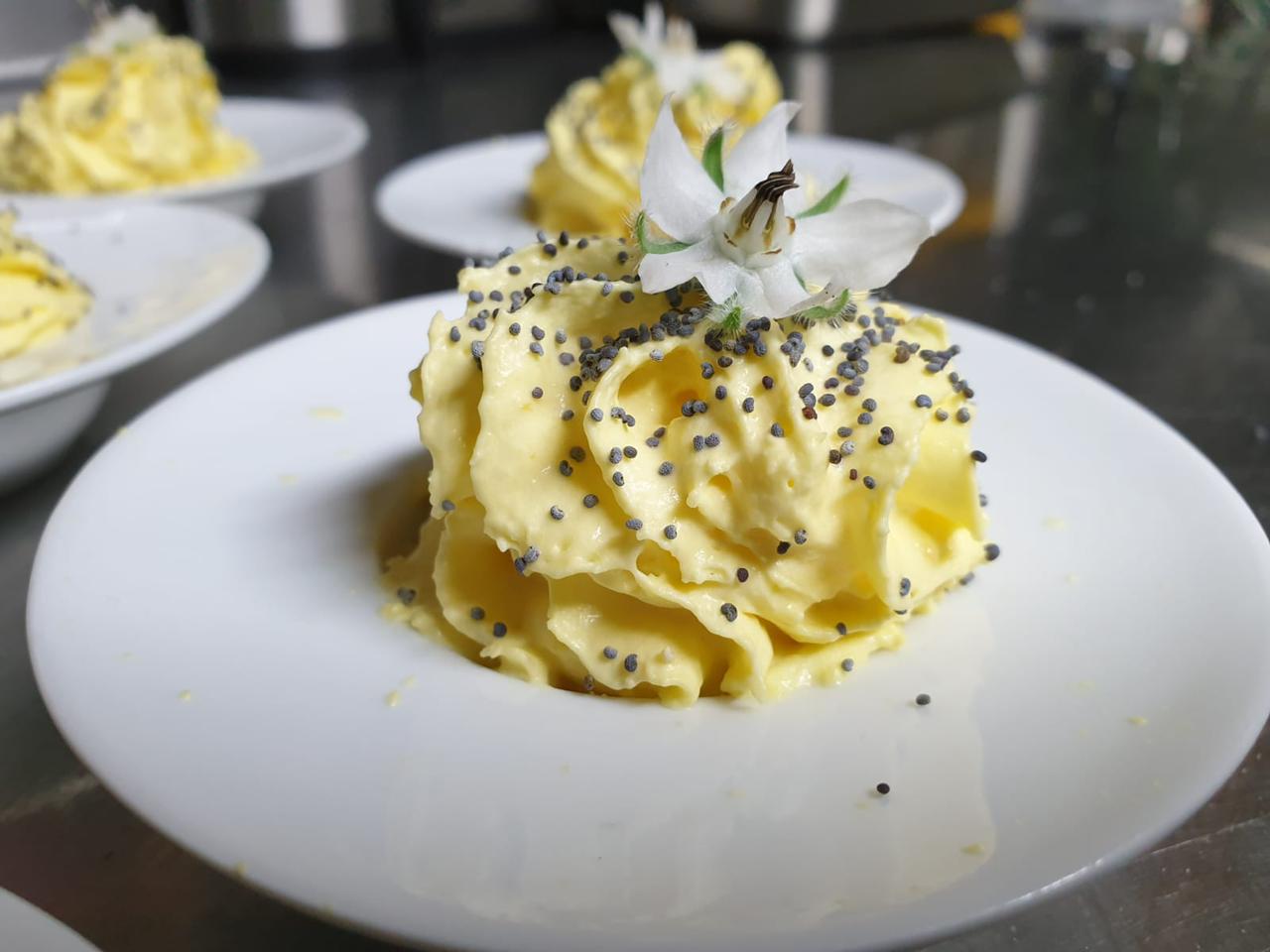 Menjar groc en un plat blanc, guarnit amb llavors negres i una flor blanca.