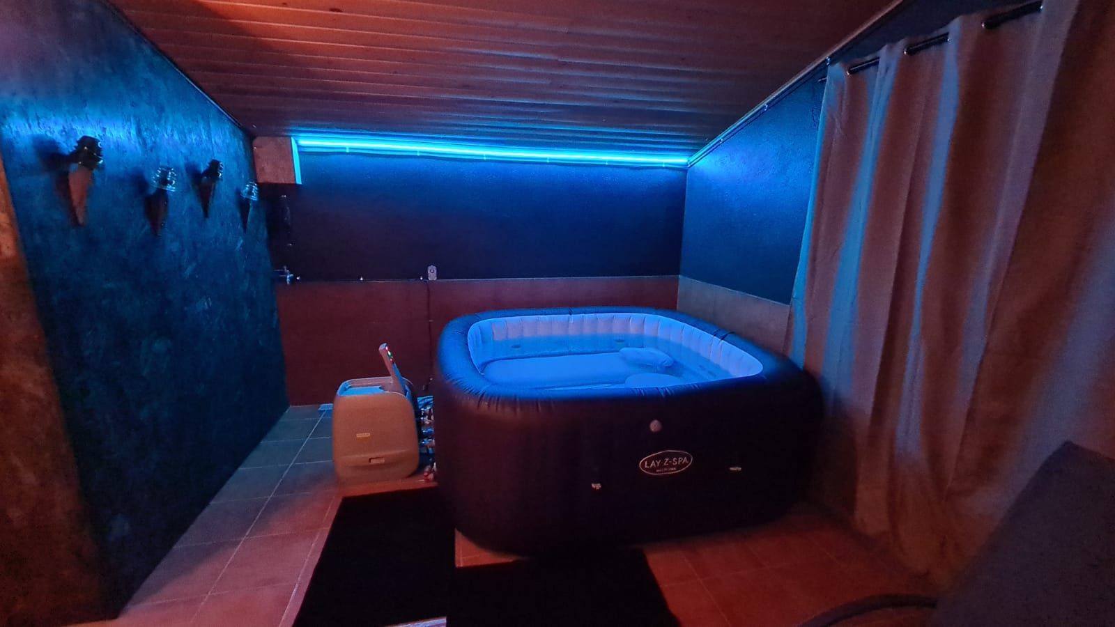 Habitació petita amb jacuzzi il·luminat, llums de neó blaus i decoració fosca. Cal Serni