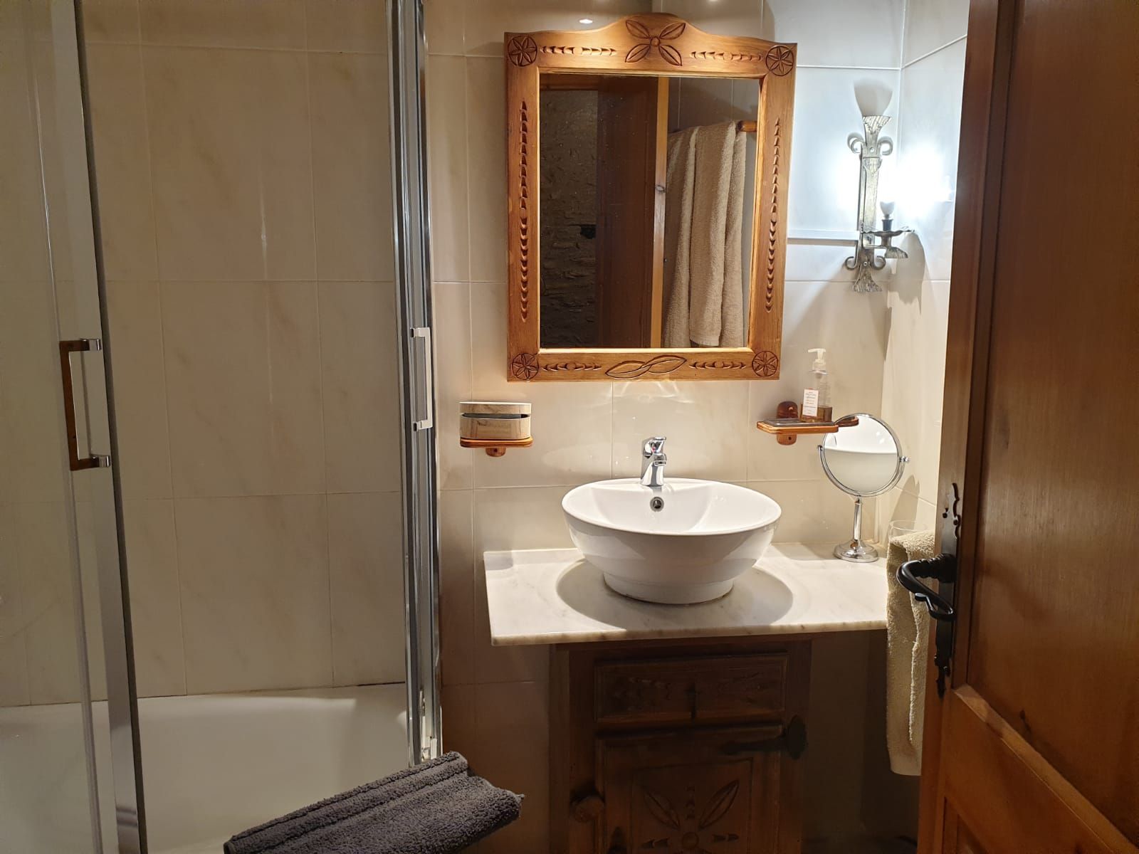 Bany amb un lavabo rodó, un mirall ornamentat i una dutxa. La porta està lleugerament entreoberta. Cal Serni