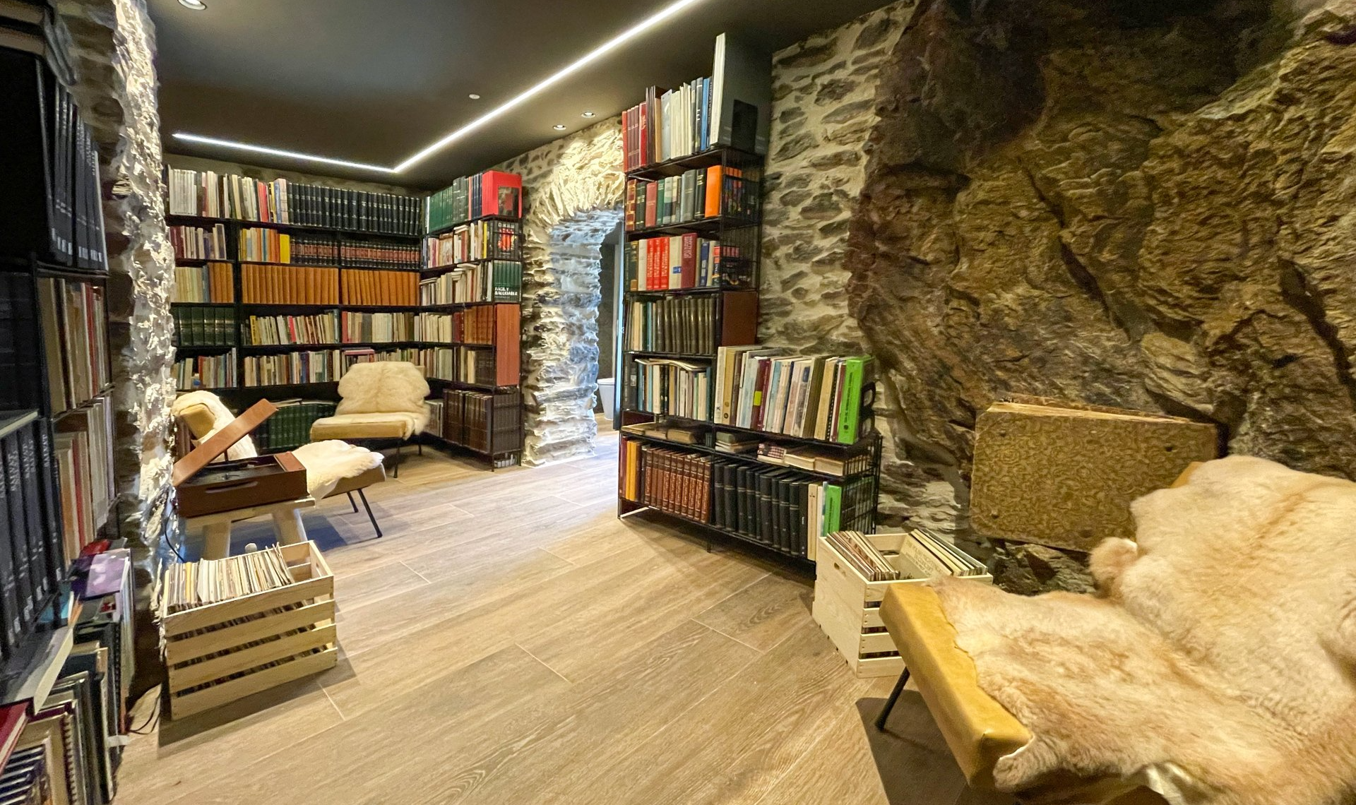 Biblioteca acollidora amb parets de pedra, prestatgeries i cadires de lectura. Cal Serni