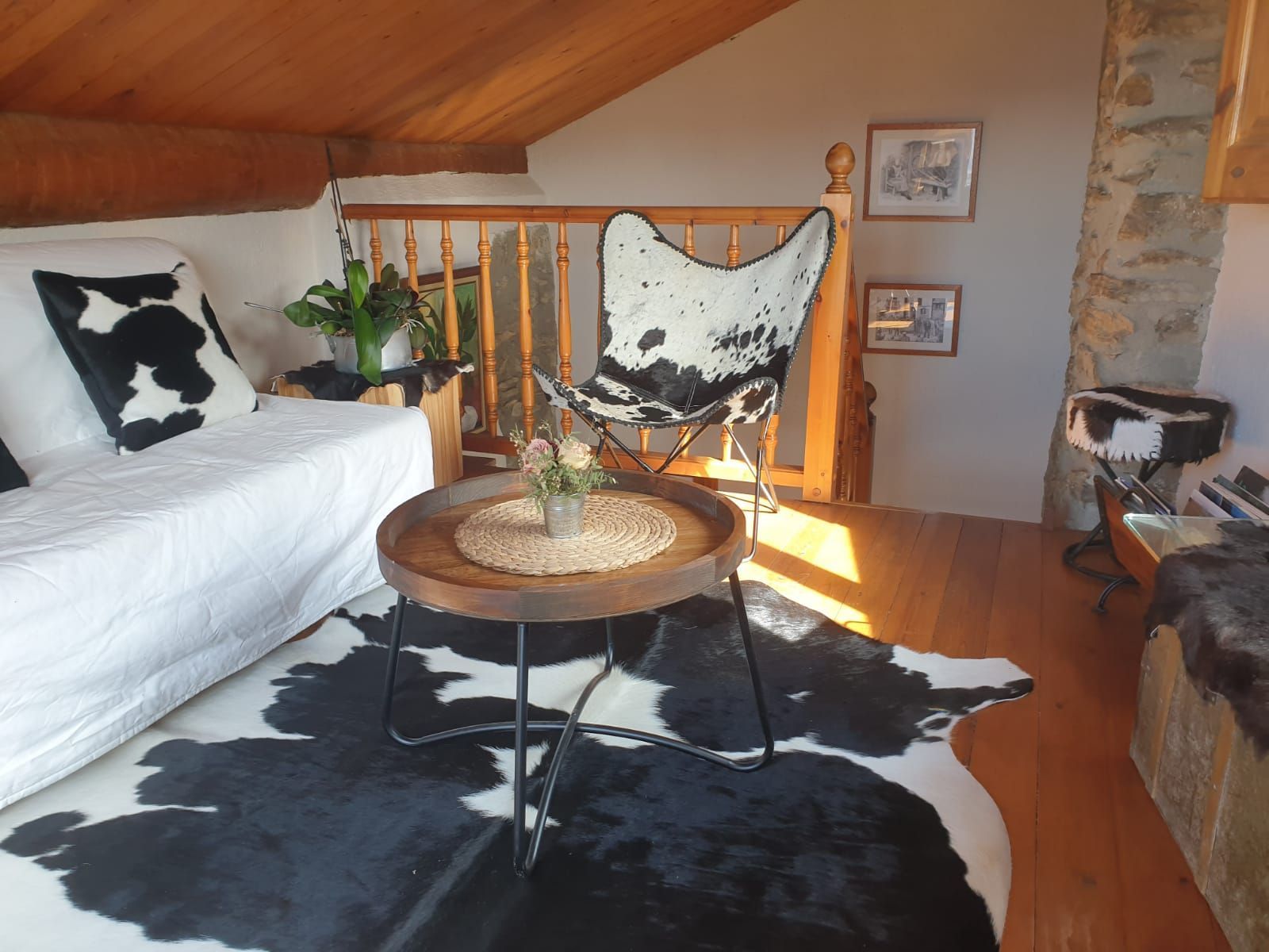 Interior acollidor d'un loft amb catifa, cadira i sofà de pell de vaca; una petita taula rodona amb plantes. 