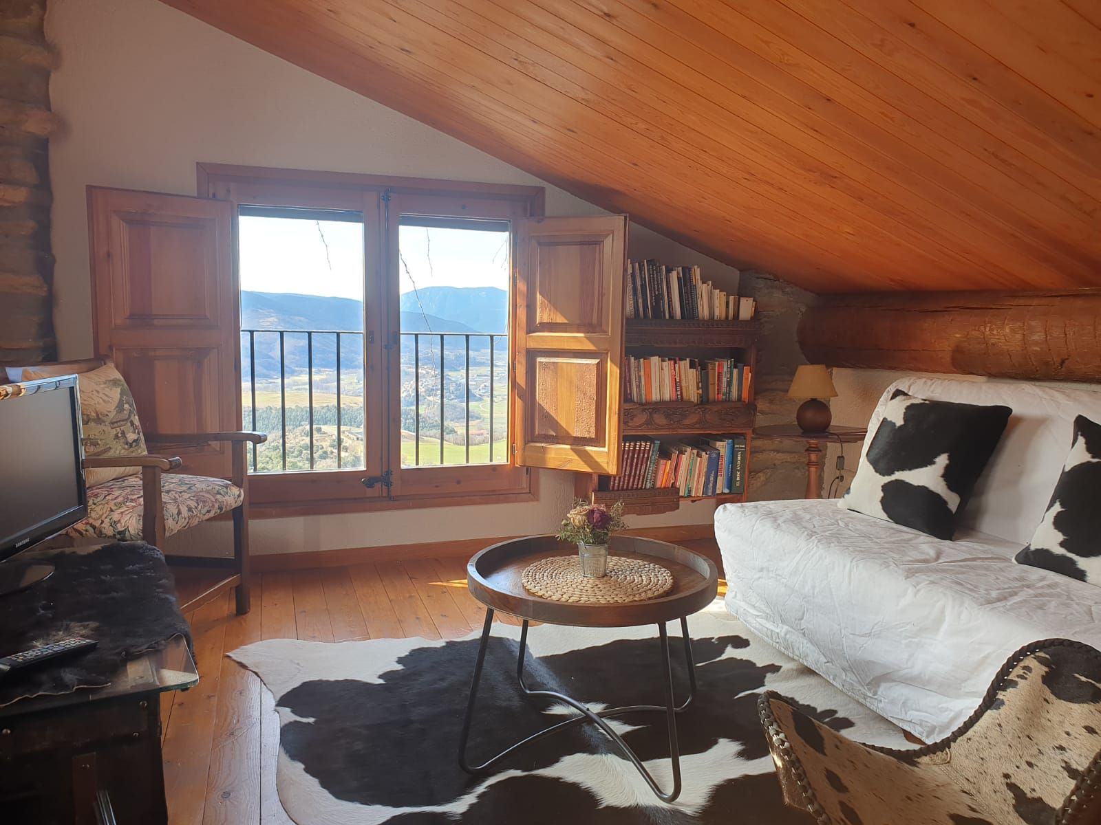 Acollidora sala d'estar a les golfes amb persianes de fusta, un petit sofà amb  vistes a les muntanyes.
