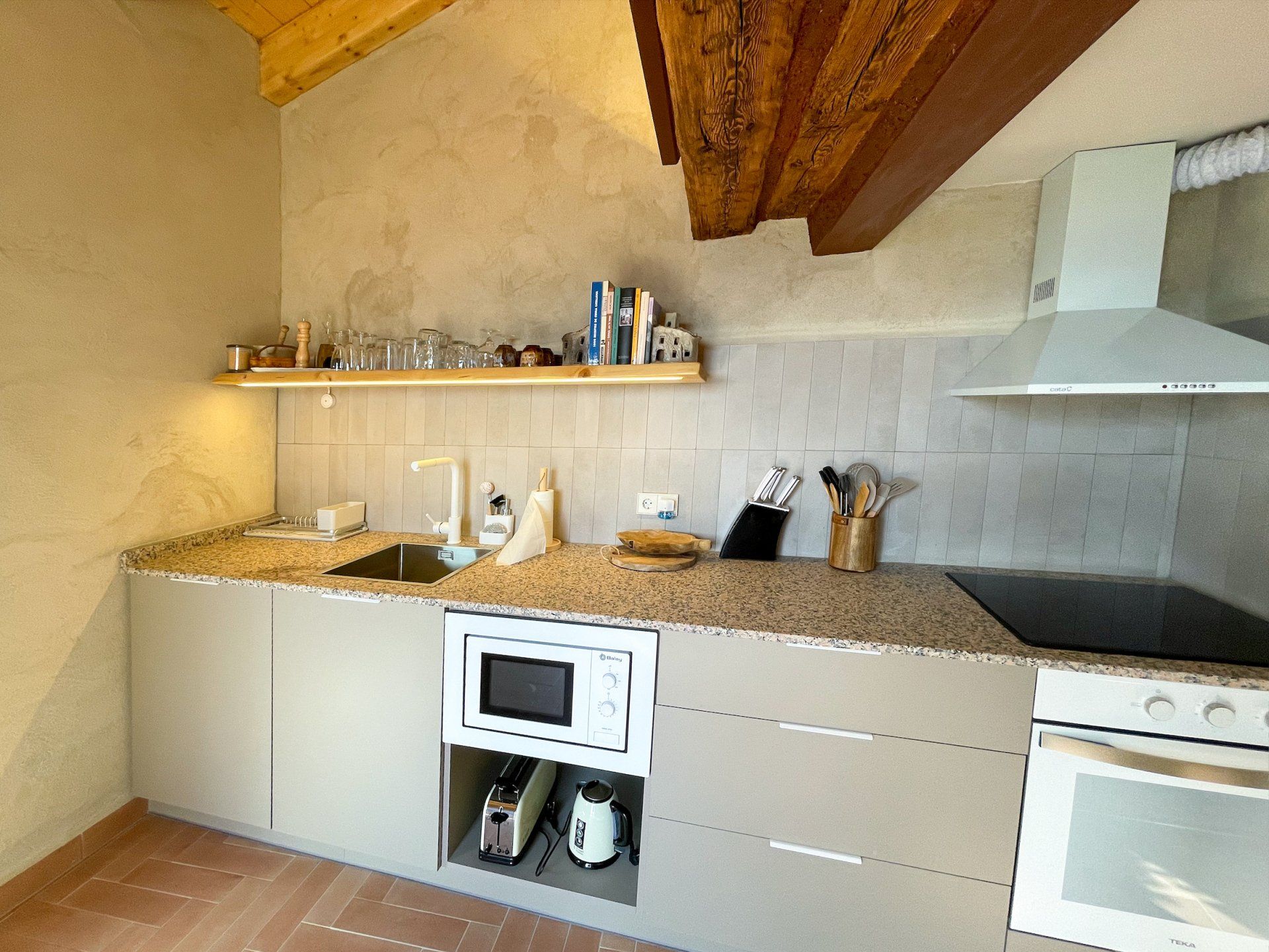 Cuina petita amb armaris beix, taulells de granit i bigues de fusta. Cal Serni