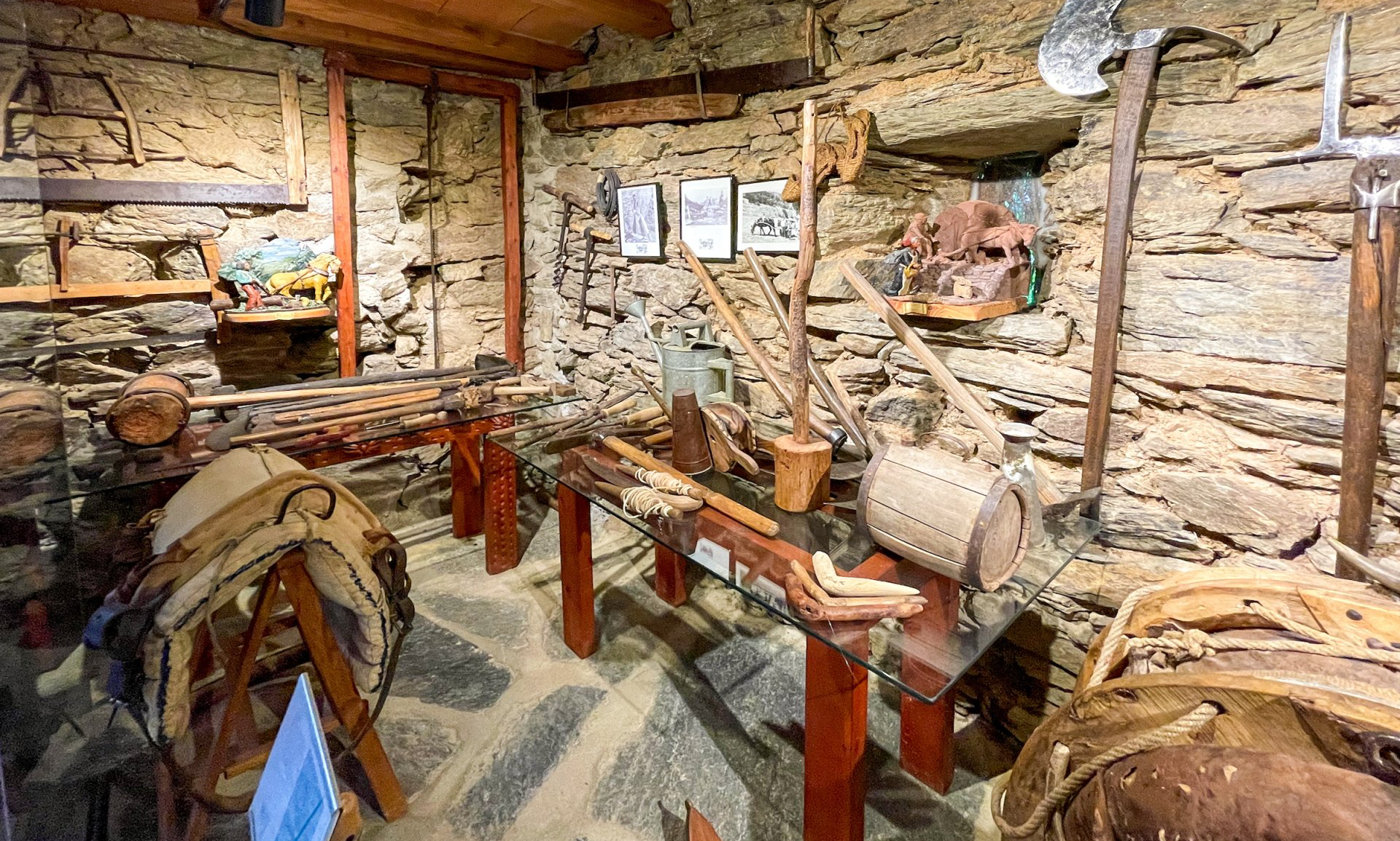 Exposició museística d'eines agrícoles antigues en una sala amb parets de pedra. Cal Serni
