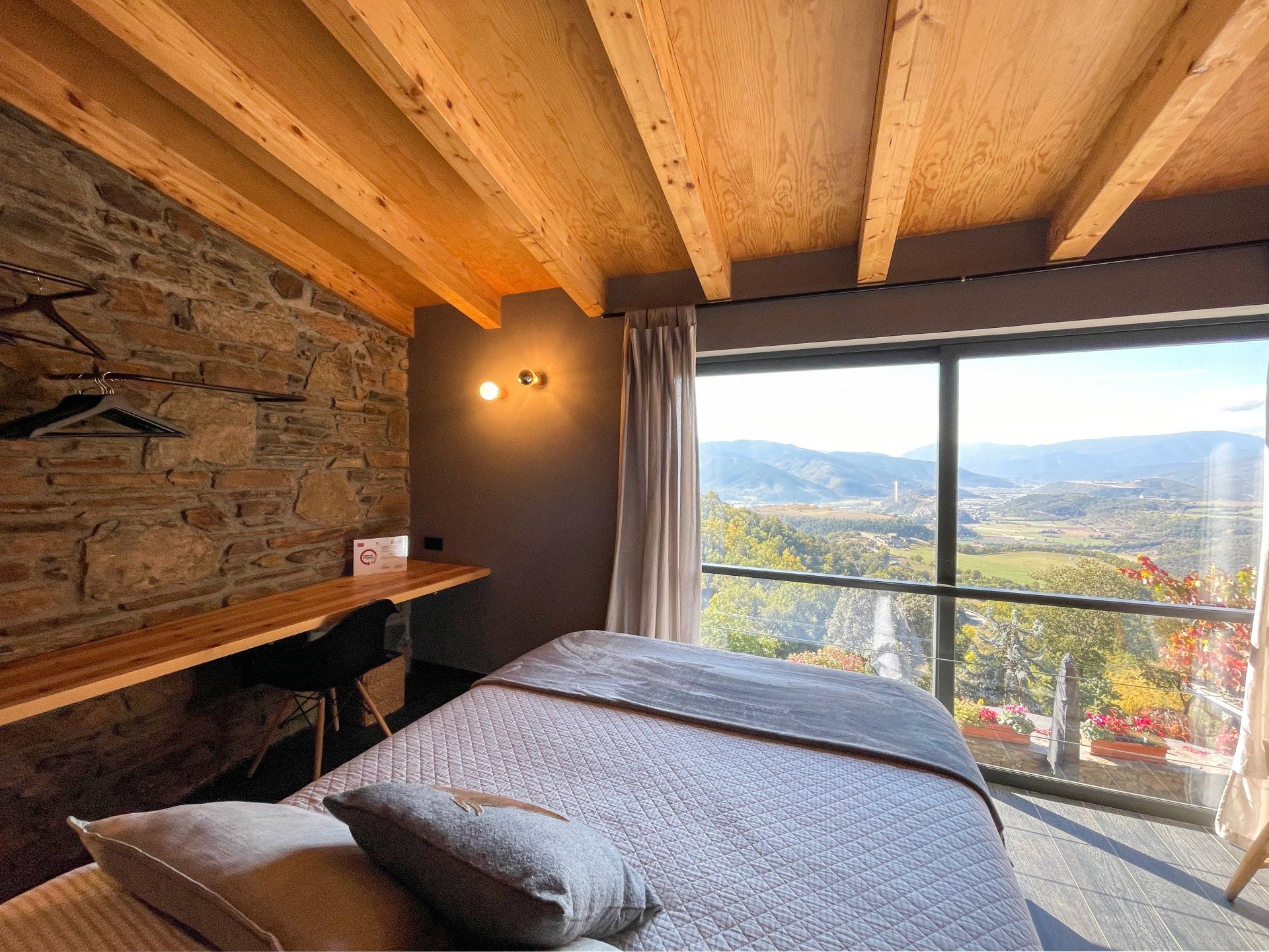 Sala de massatges amb paret de pedra, sostre de fusta i una gran finestra amb vistes a una vall. Cal Serni