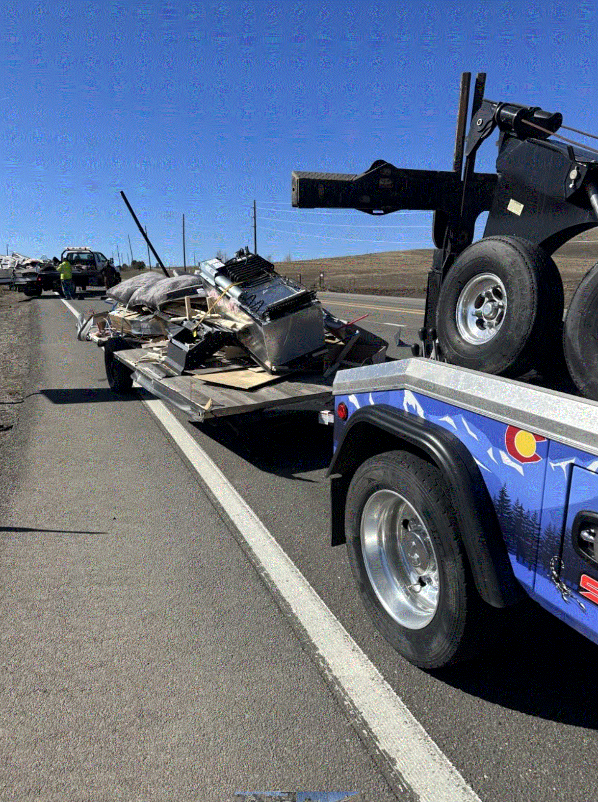Tow truck on a road hauling debris from an accident; sunny day with a blue sky.