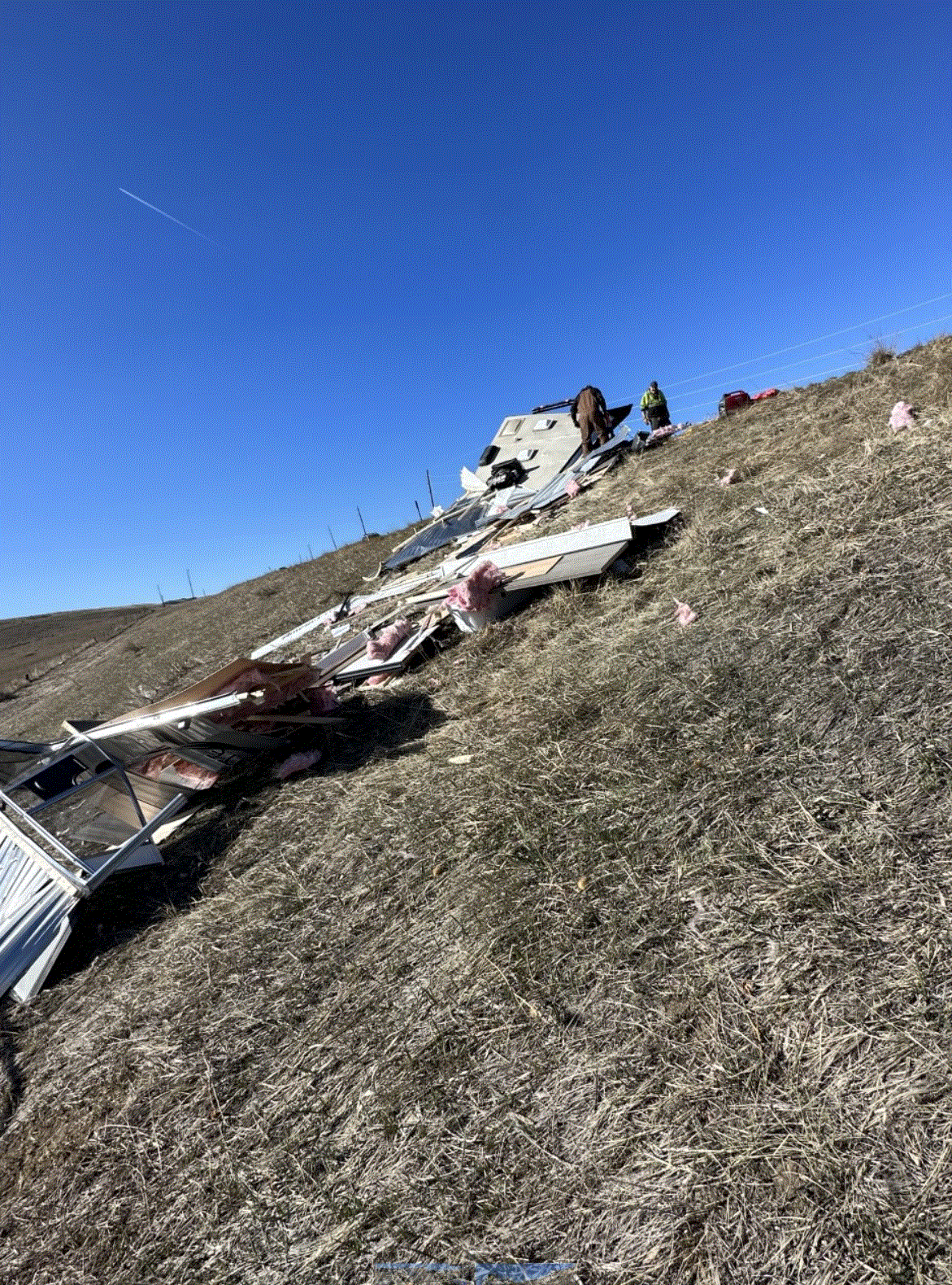 Plane wreckage scattered on a grassy hillside under a clear blue sky.