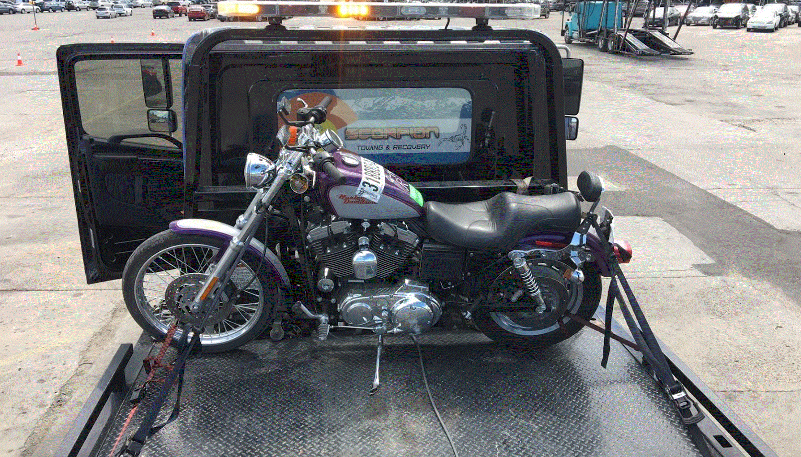 Motorcycle on a tow truck. The bike is purple and silver. Tow truck is black. Outdoors.