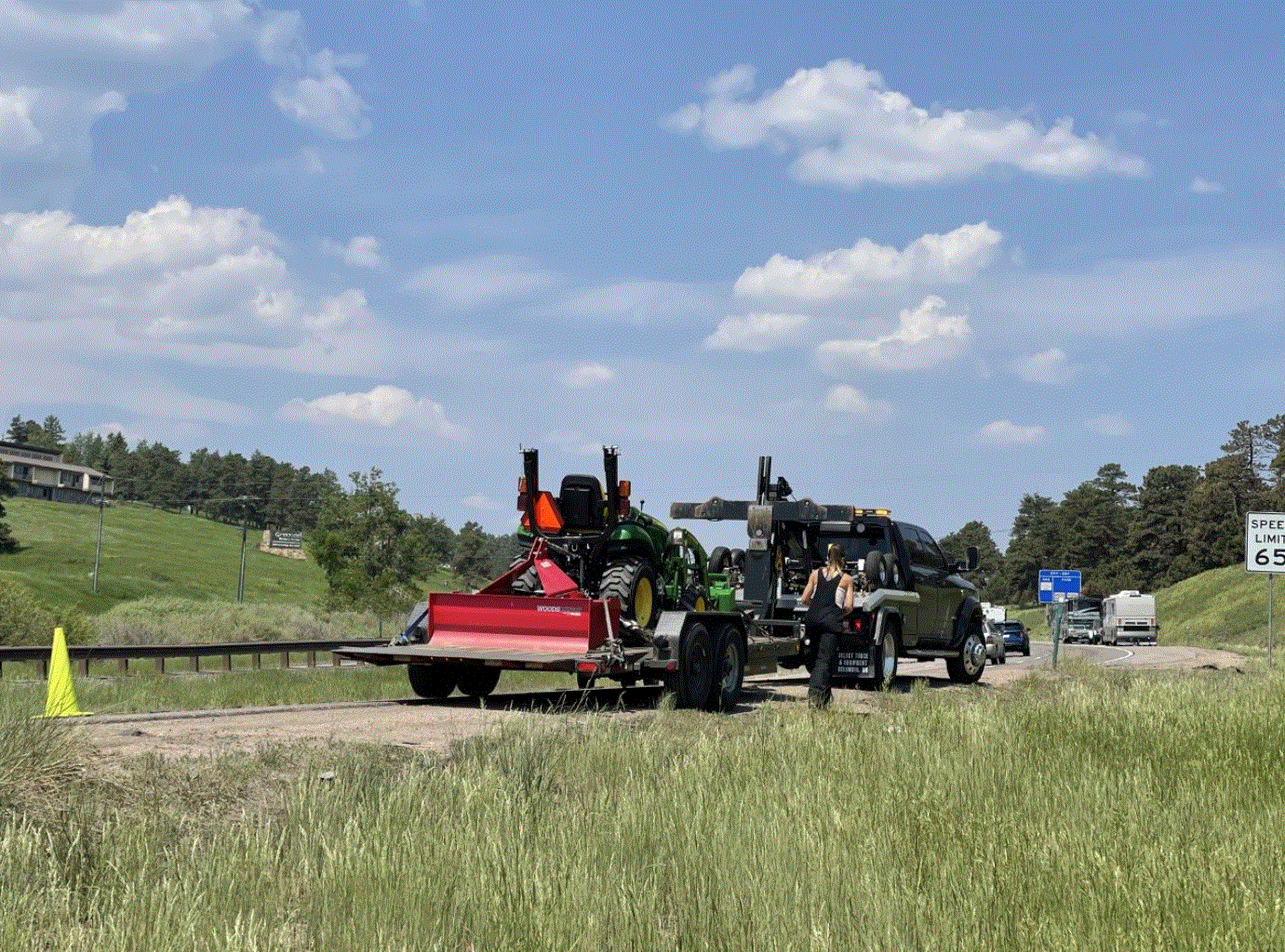 A truck and trailer with a tractor on it parked on the side of a road.