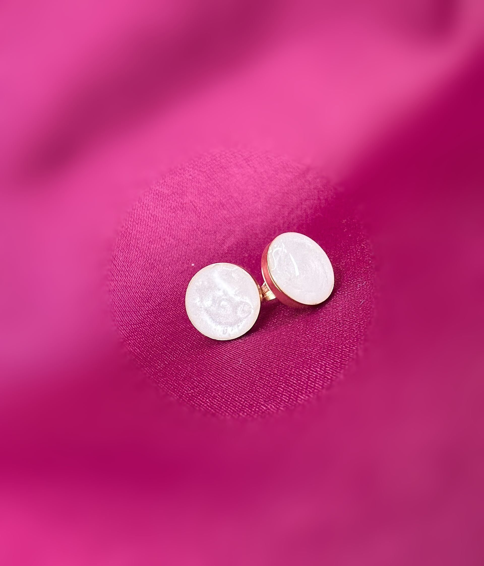 White pumpkin-shaped bowl filled with dark purple beads, with two white round pieces in front, on a pink background