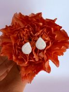 Orange paper flower with two white teardrop decorations in the center, held in a hand