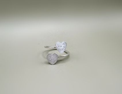 Silver ring with two heart-shaped stones, one clear and one pale pink, on a light background