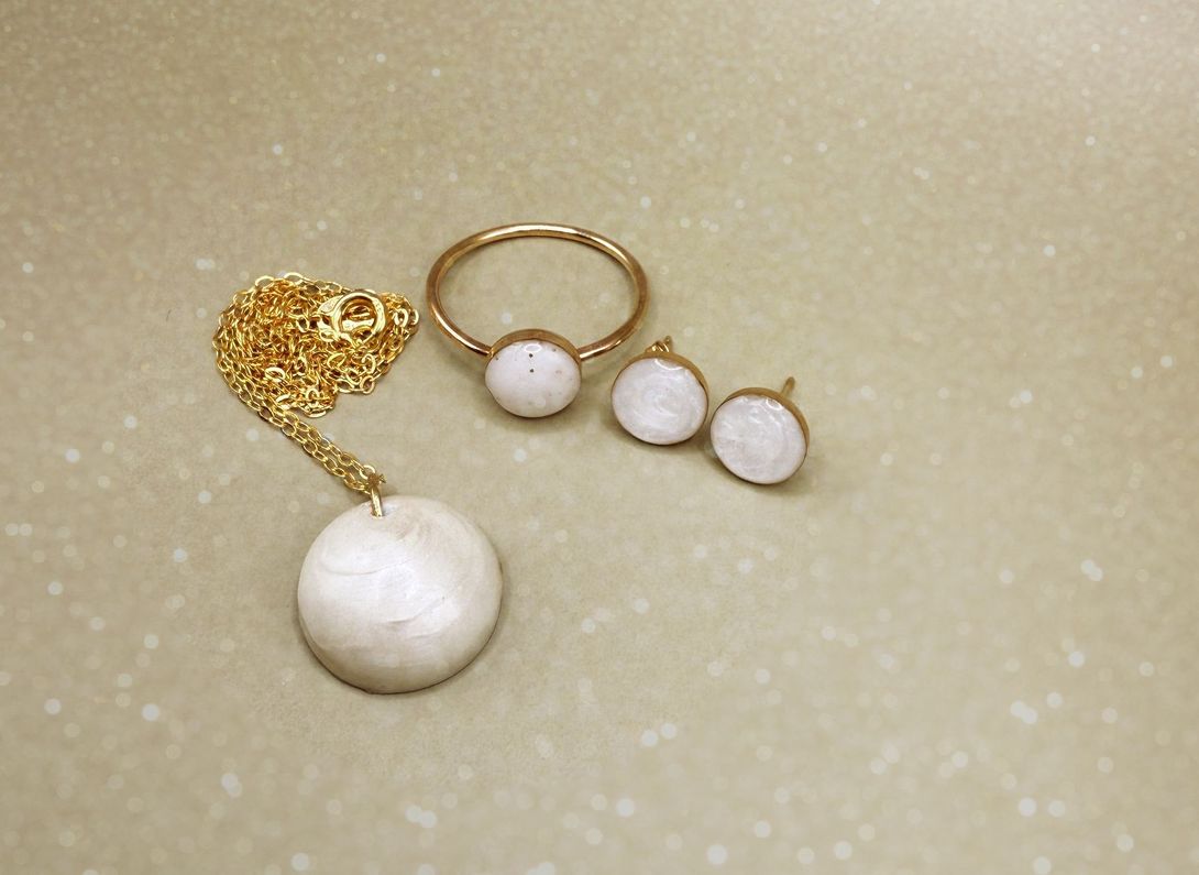 Gold necklace and pearl earrings arranged on a beige surface