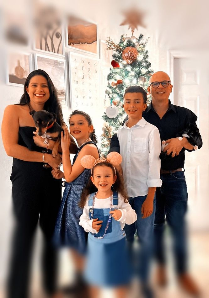 My family Family gathered indoors in front of a decorated tree, smiling and holding a small dog.
