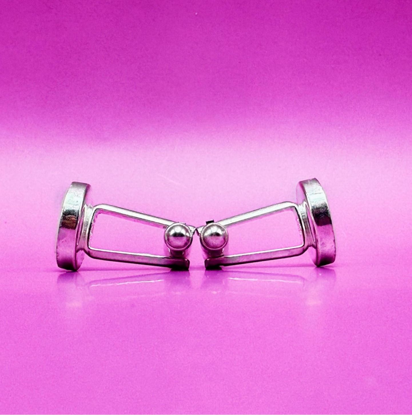 Pair of silver cufflinks with beige round fronts on a pink background