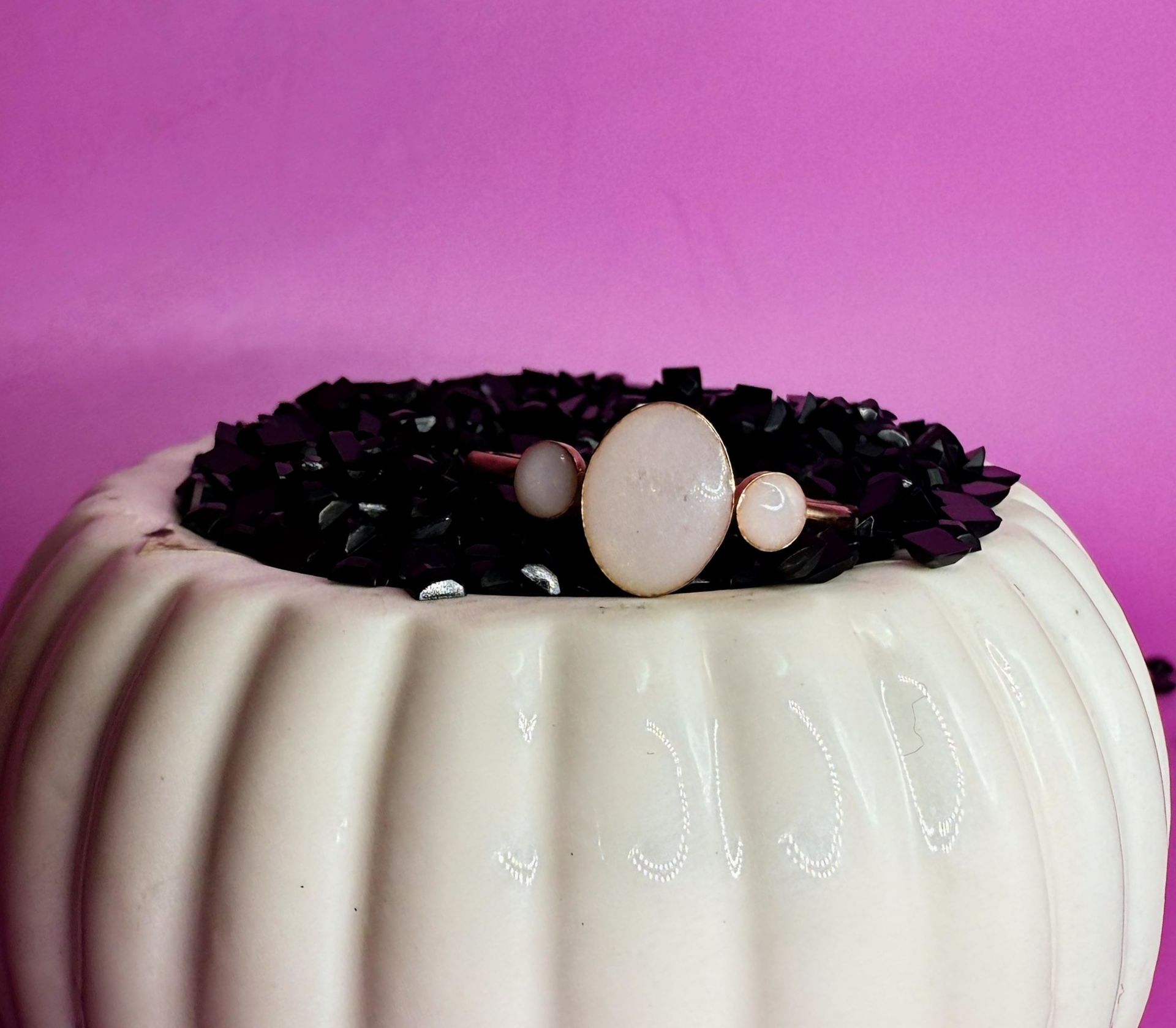 White ribbed candle with black wax and pearl-like beads on top against a pink background