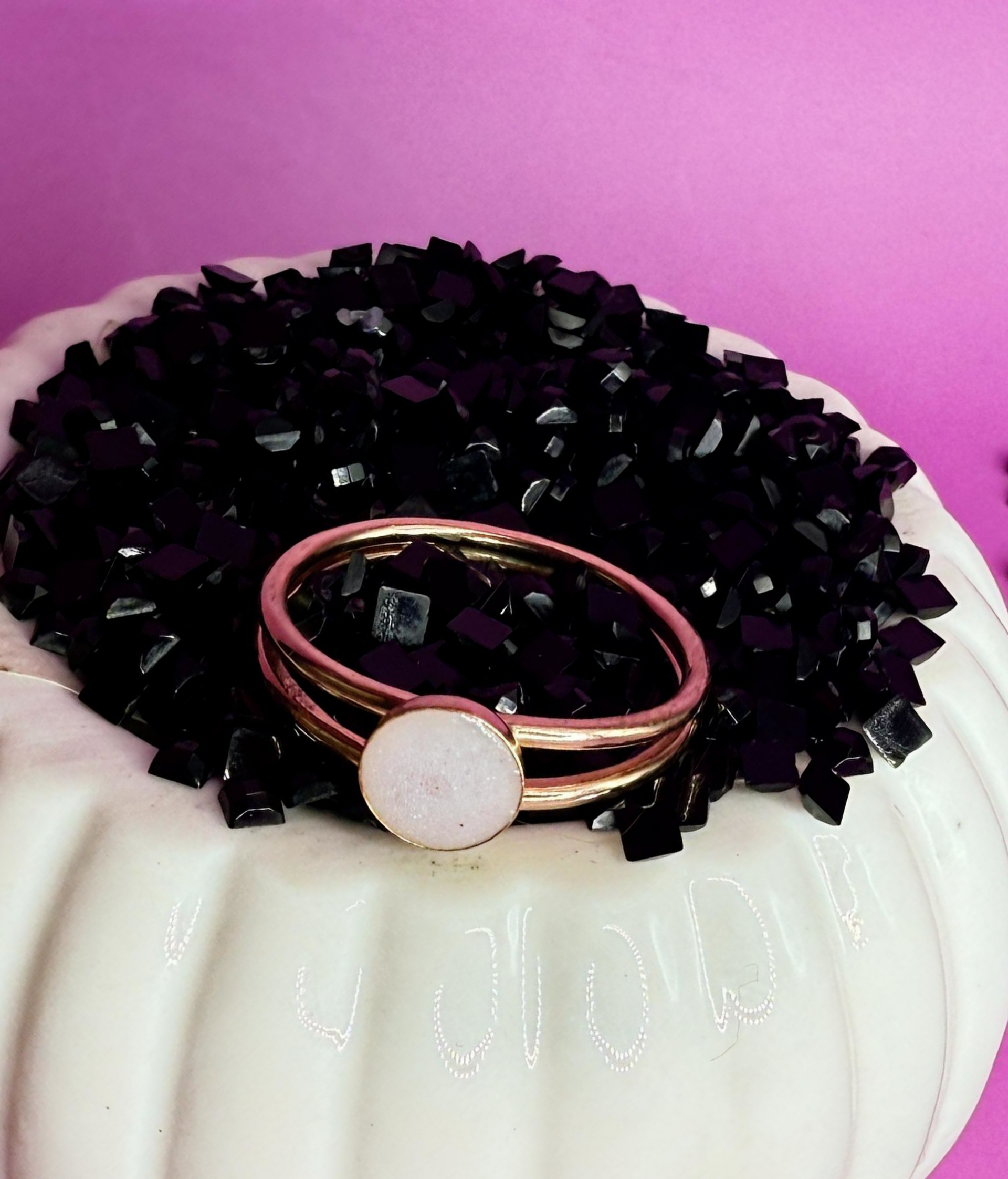 Rose gold rings on a white stand with a black beaded crown and pink background