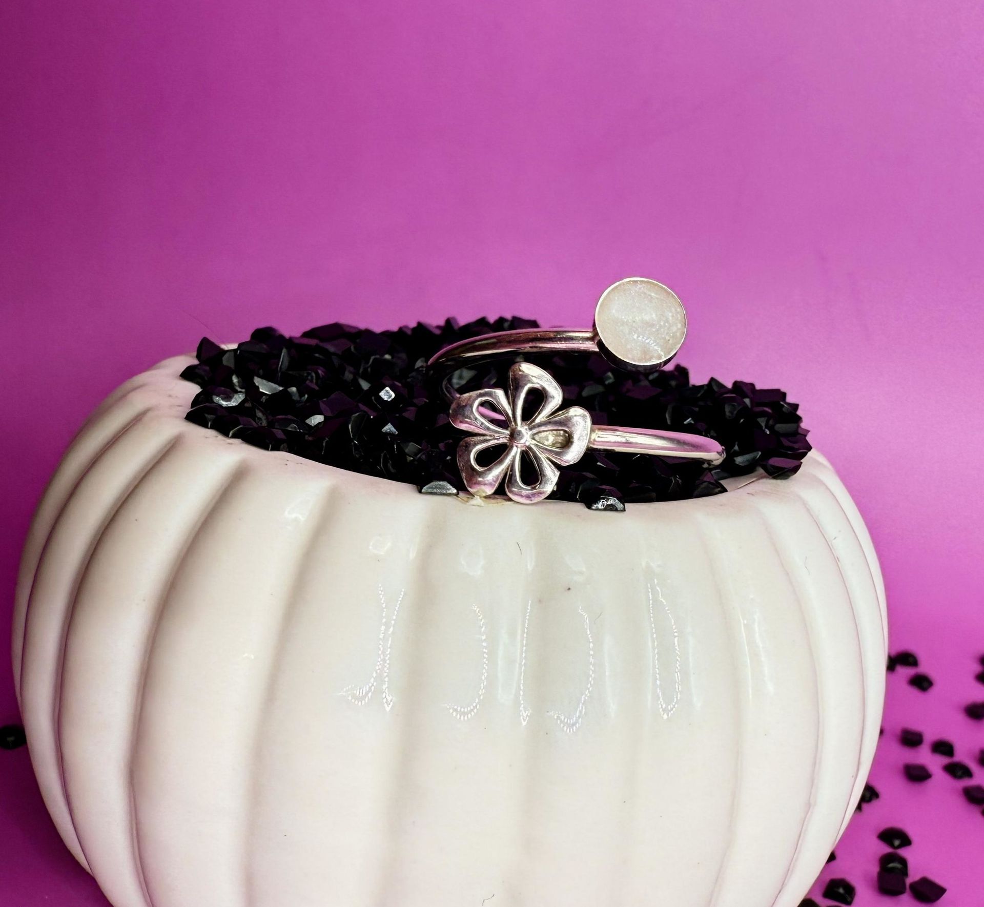 White ribbed vase with black stones and silver flower rings on a pink background