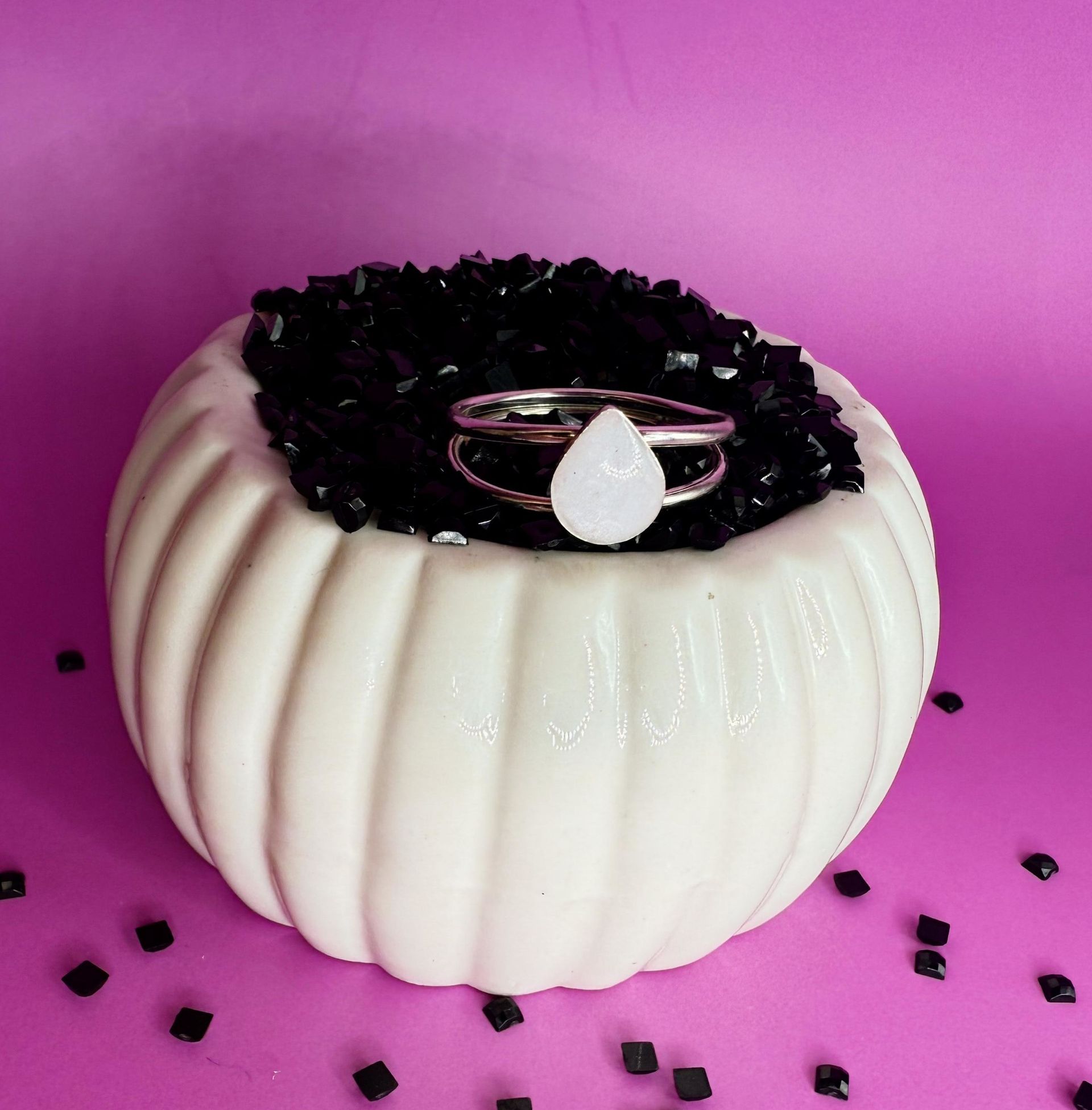 White pumpkin-shaped trinket box with black top and silver ring on a pink background