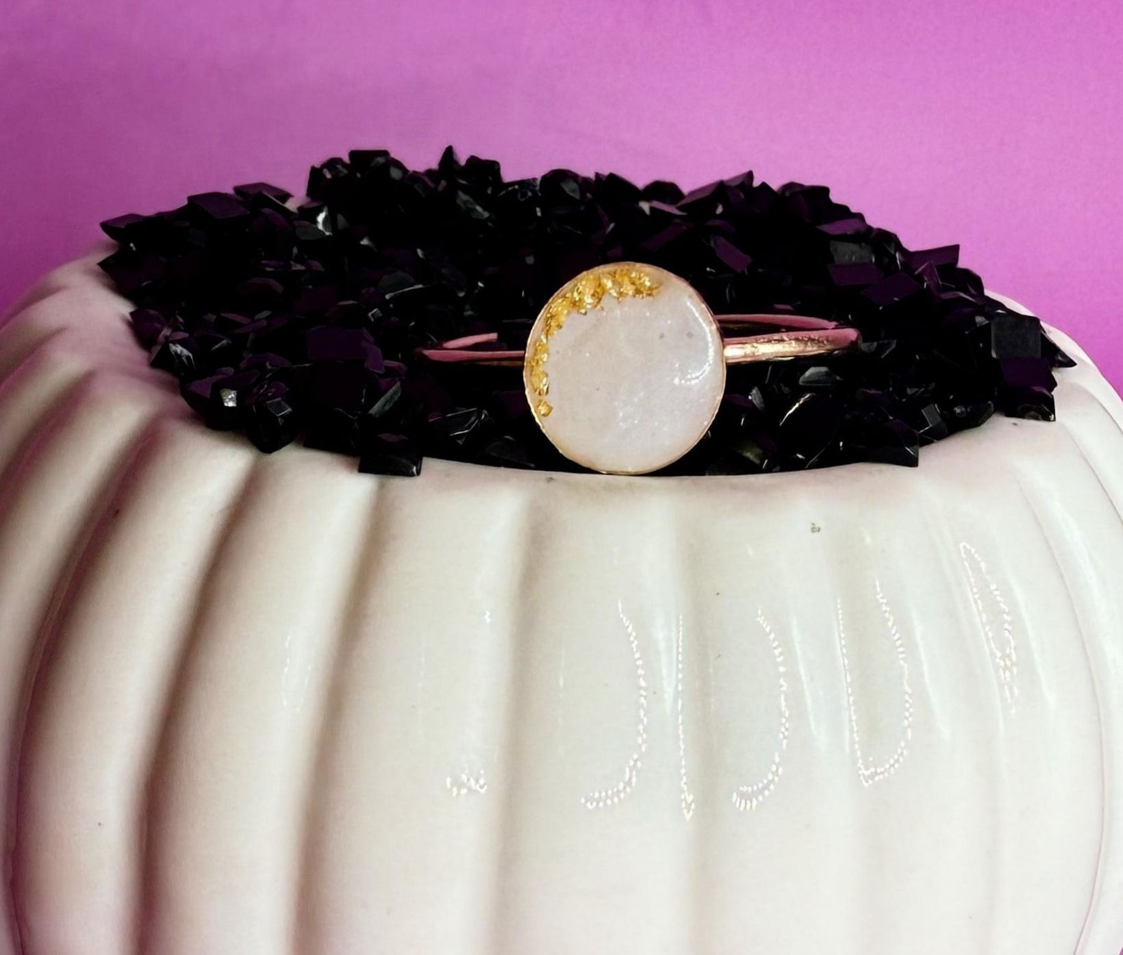 White cake with black topping and a gold-rimmed pearl accent on a pink background