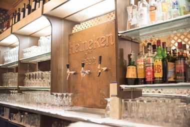 Bar con spine di birra Heineken, bicchieri e bottiglie di liquore sugli scaffali.