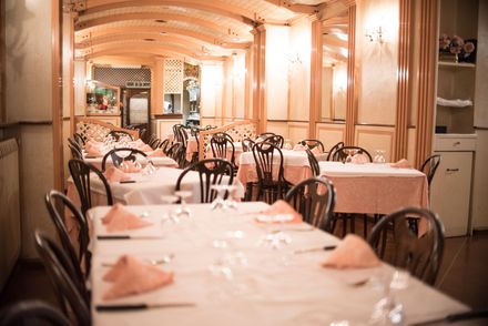 Interno di un ristorante con tavoli apparecchiati per la cena, tovaglie e tovaglioli color pesca, rivestimenti in legno.