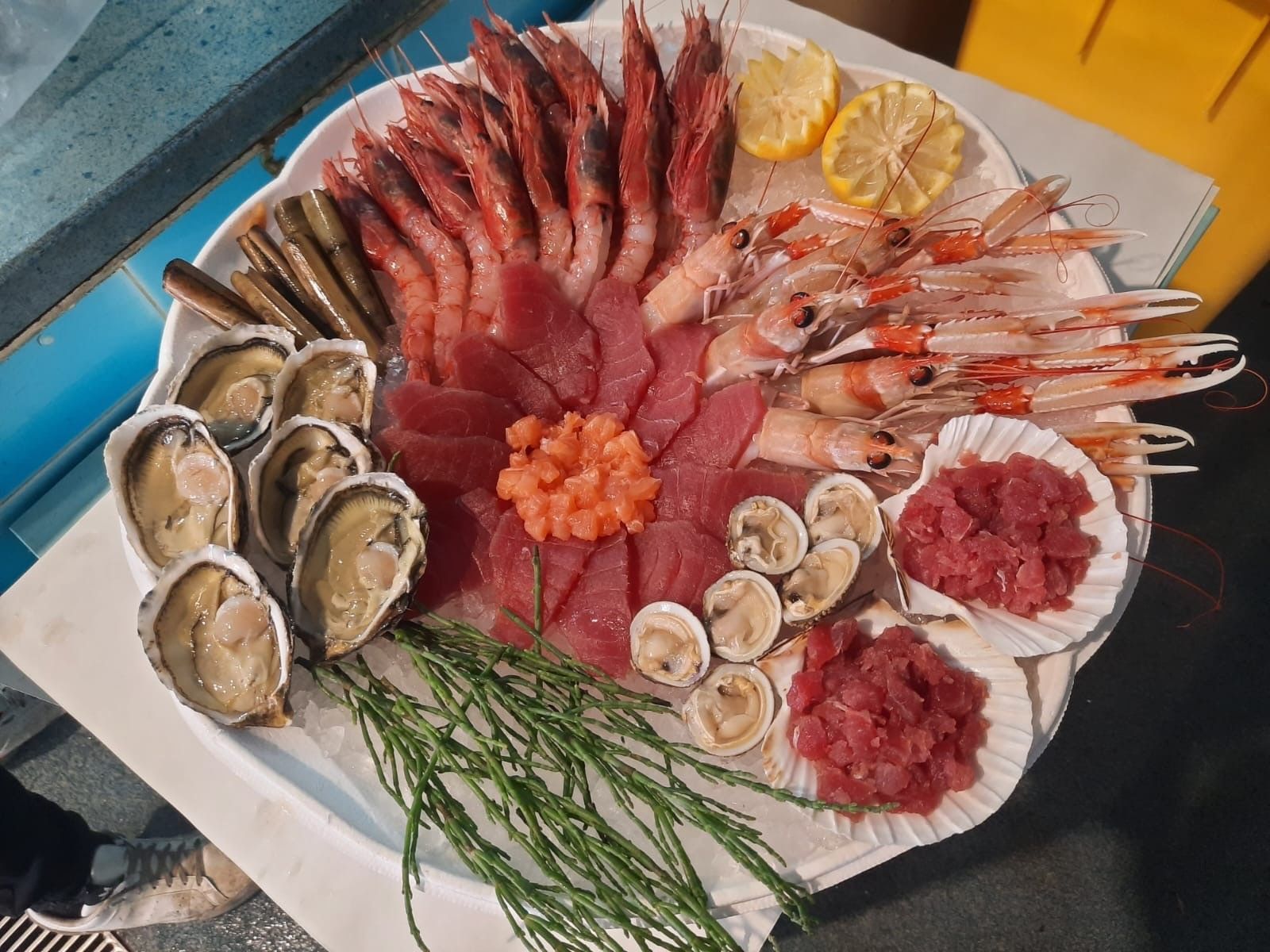 Piatto di frutti di mare con gamberi, ostriche, tonno, vongole e spicchi di limone.