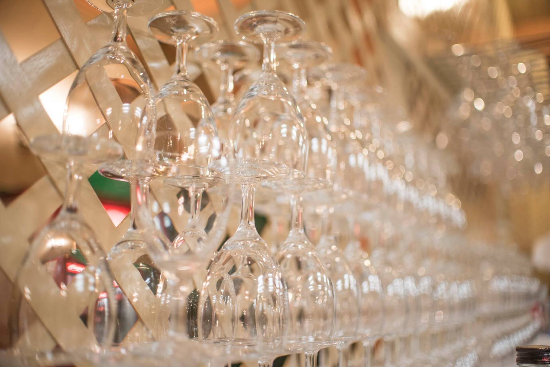 File di bicchieri da vino capovolti appesi a una rastrelliera di legno, all'interno di un ristorante.