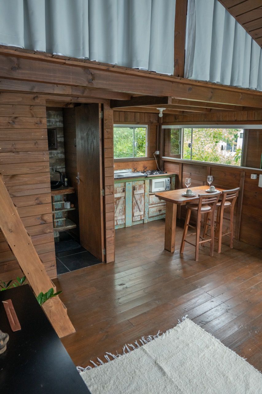 Interior rústico de loft em madeira com uma pequena mesa, bancos, janelas e uma escada.