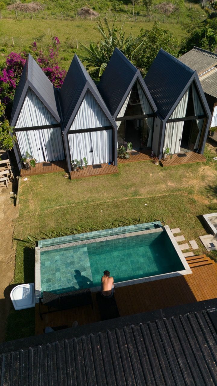 Vista aérea de pequenas cabanas ao lado de uma piscina no quintal, com uma pessoa nadando na água.