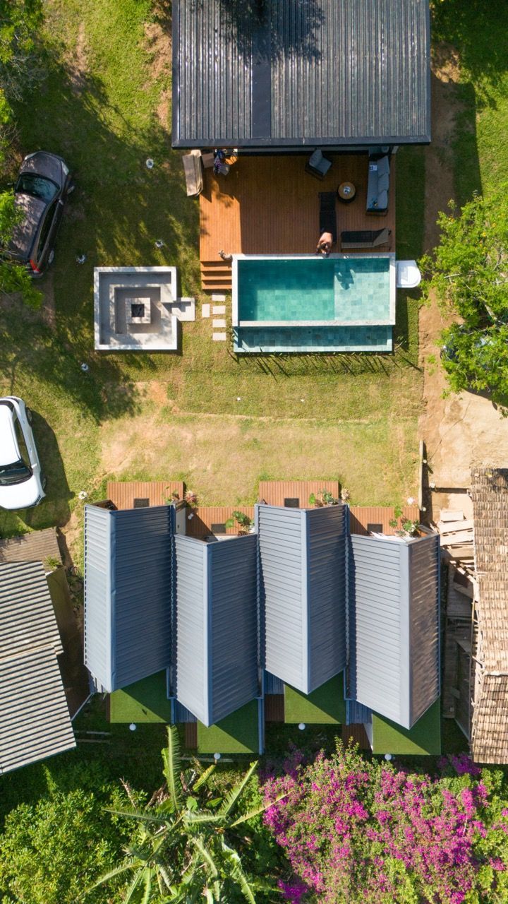 Vista aérea de um quintal com piscina, pátio e pequenas cabanas ao lado de grama verde e árvores.