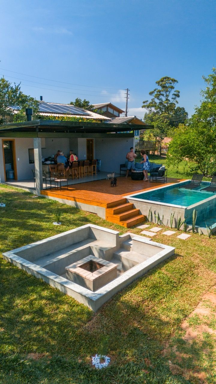 Pátio nos fundos com uma pequena piscina, degraus de tijolos e pessoas sentadas sob um telhado que proporciona sombra.