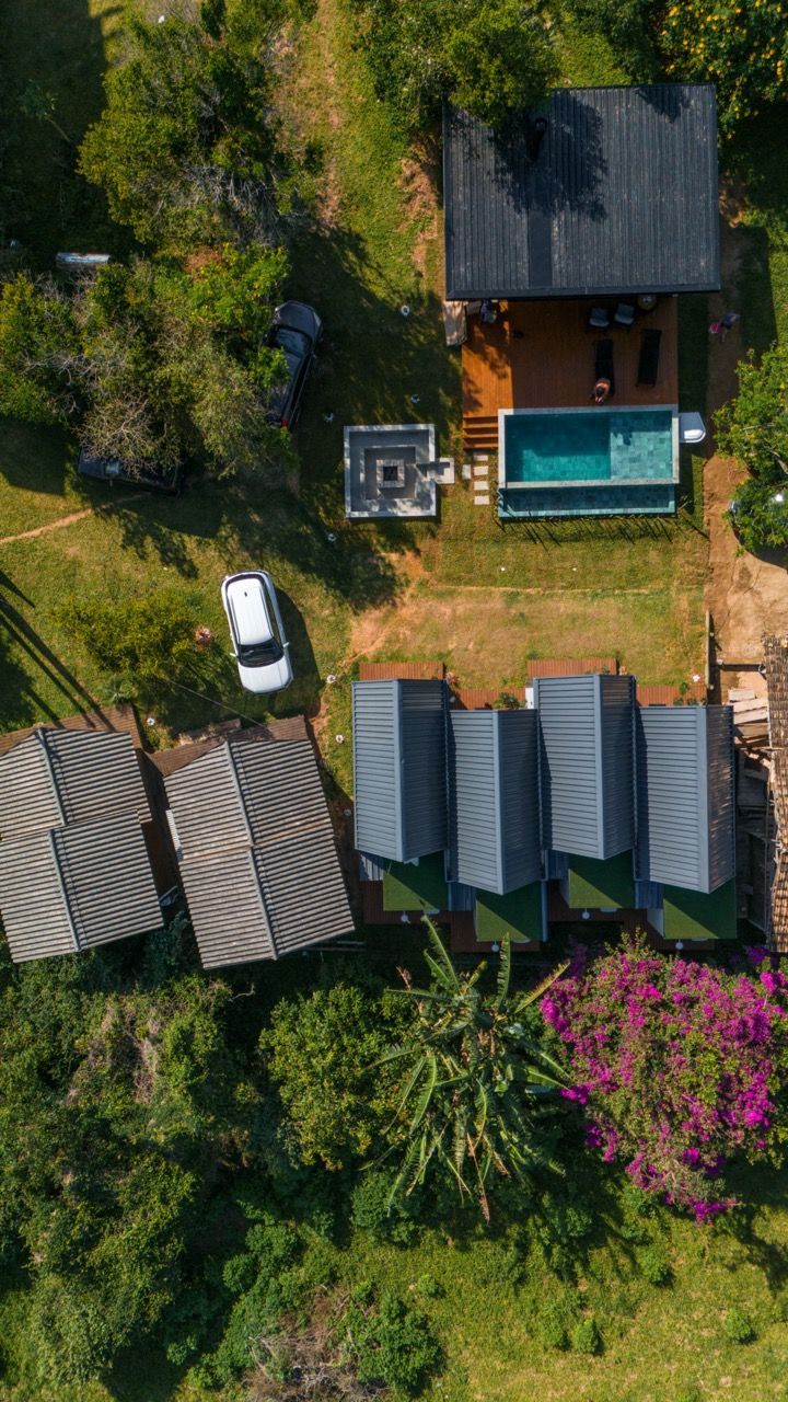Vista aérea de uma casa com piscina, carro branco e um jardim verdejante.