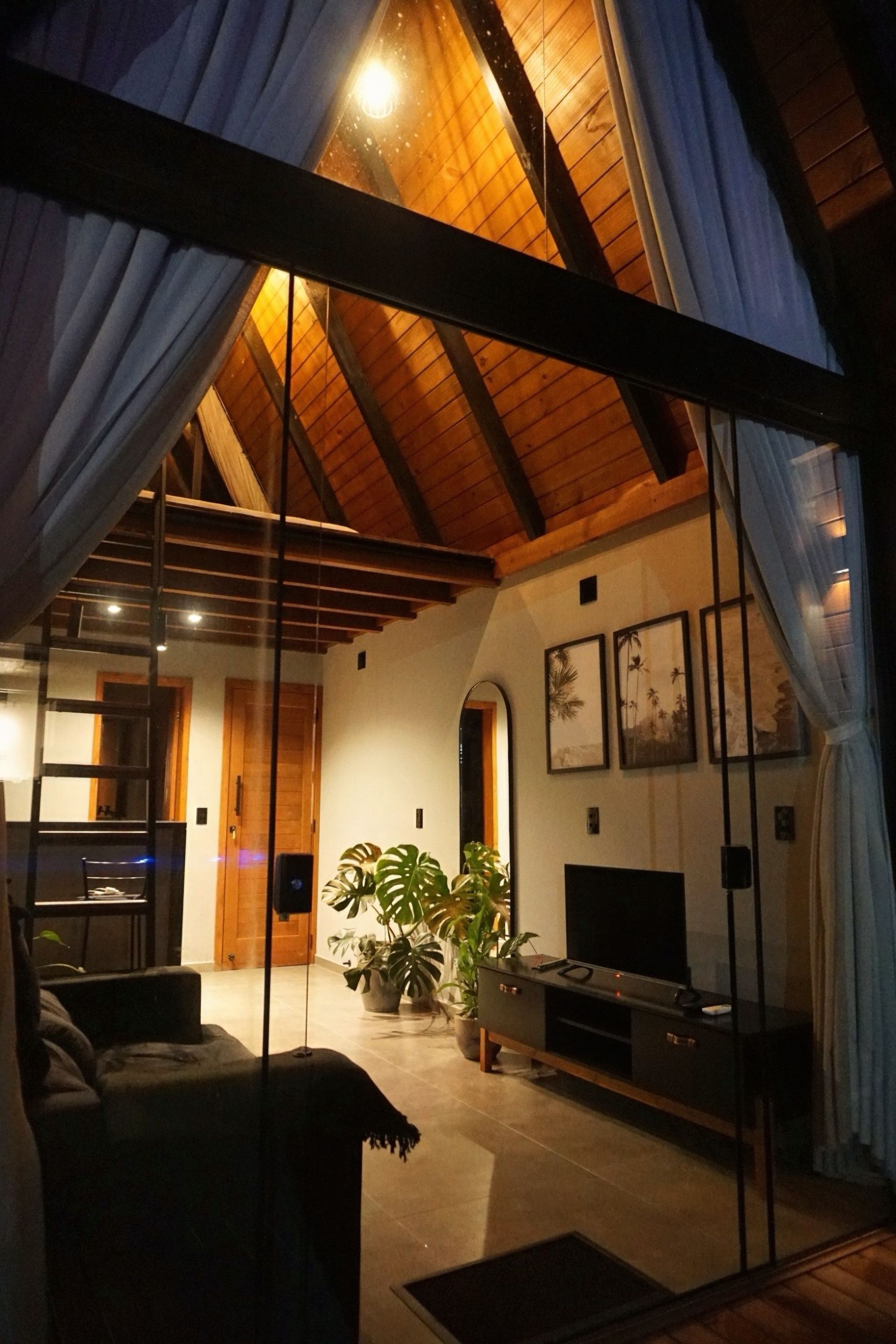 Sala de estar aconchegante com teto abobadado de madeira, cortinas azuis, iluminação quente e mobília moderna.