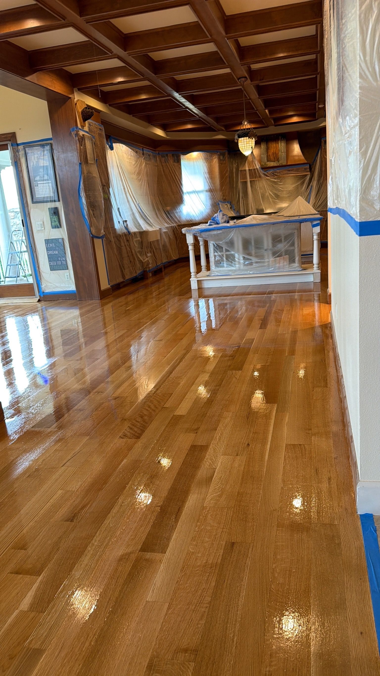 Renovated room with glossy wood floor, exposed ceiling beams, and plastic-covered furniture near windows