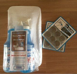 A wood floor cleaning kit with blue bottles and a white cloth, next to two packages of brown felt furniture pads.