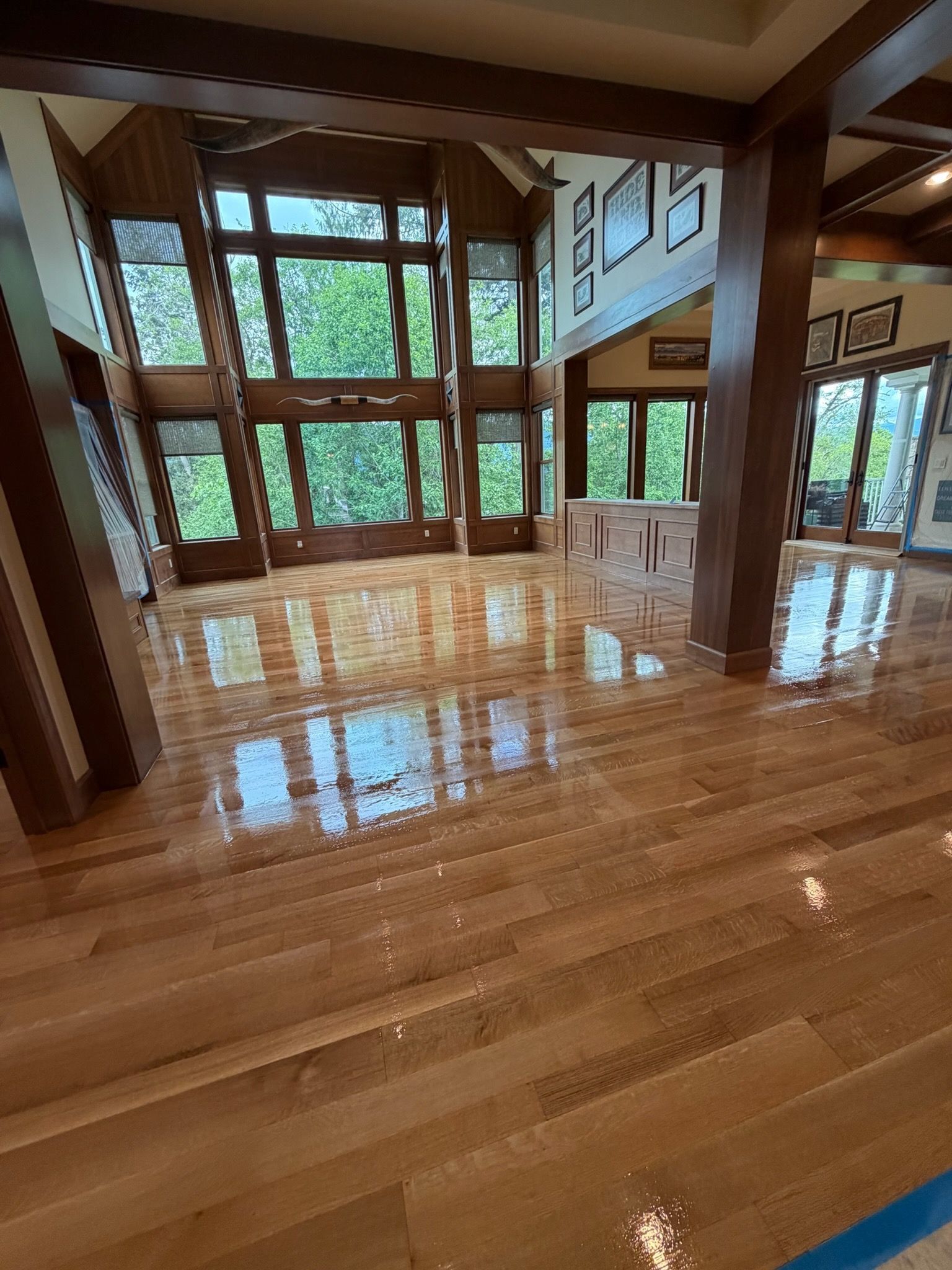 Spacious sunlit living room with polished hardwood floors, large windows, and a stone fireplace