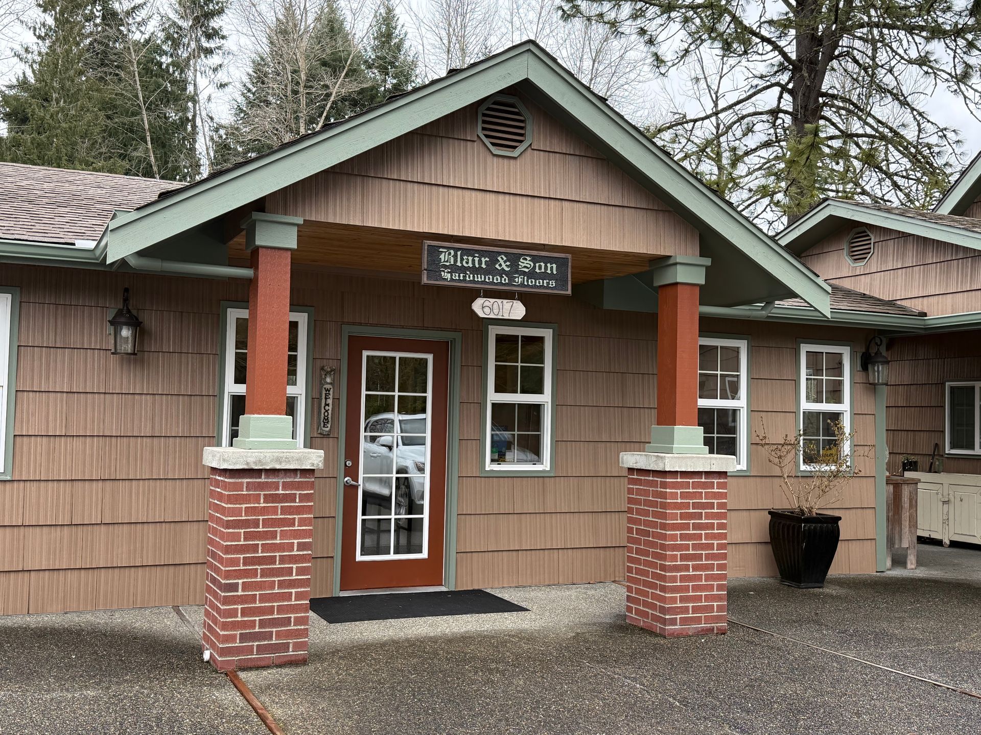 A brown, wood-shingled building with a porch, brick pillars, and a sign reading