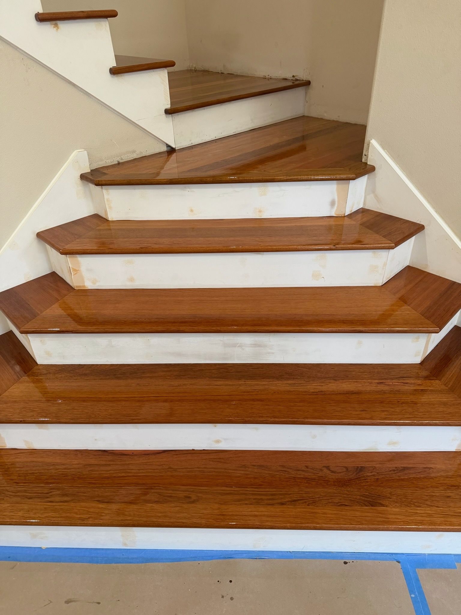 Wooden staircase with white risers and a blue-taped edge at the bottom.