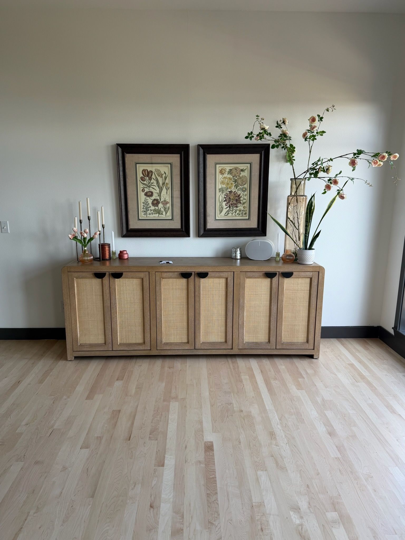 Wooden sideboard with framed art and vases against a white wall in a minimalist room