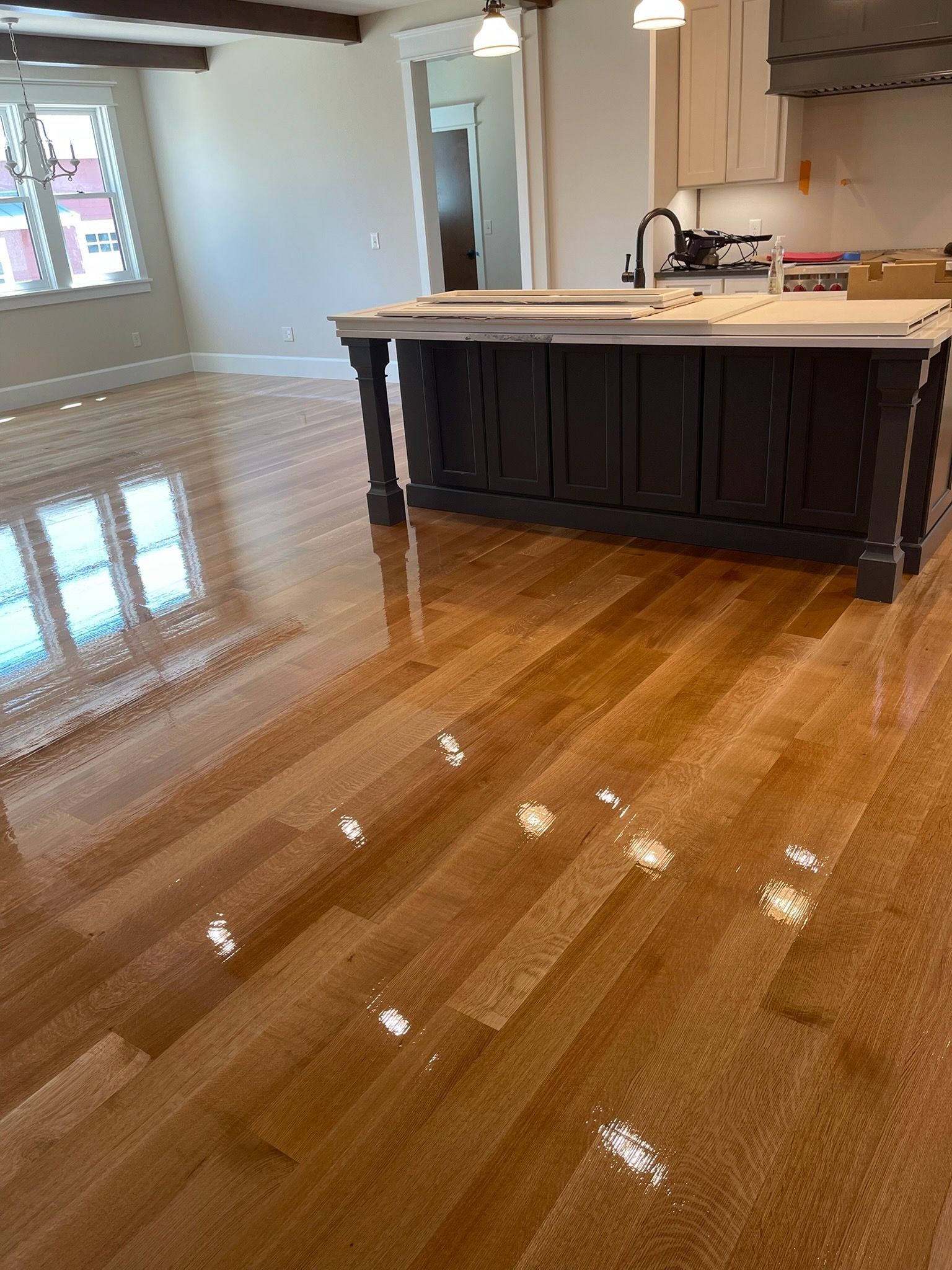 A kitchen featuring a dark wooden island with a white countertop set on a polished, light-brown hardwood floor.