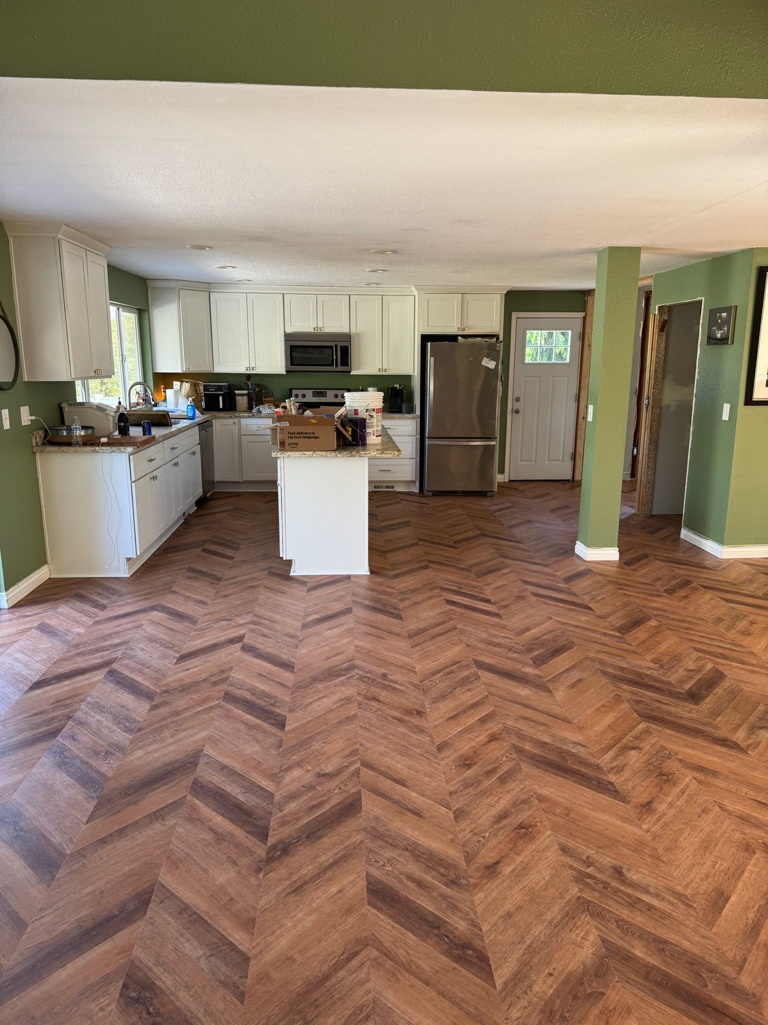 A kitchen with white cabinets, a central island, and stainless steel appliances over a brown, herringbone-pattern floor.